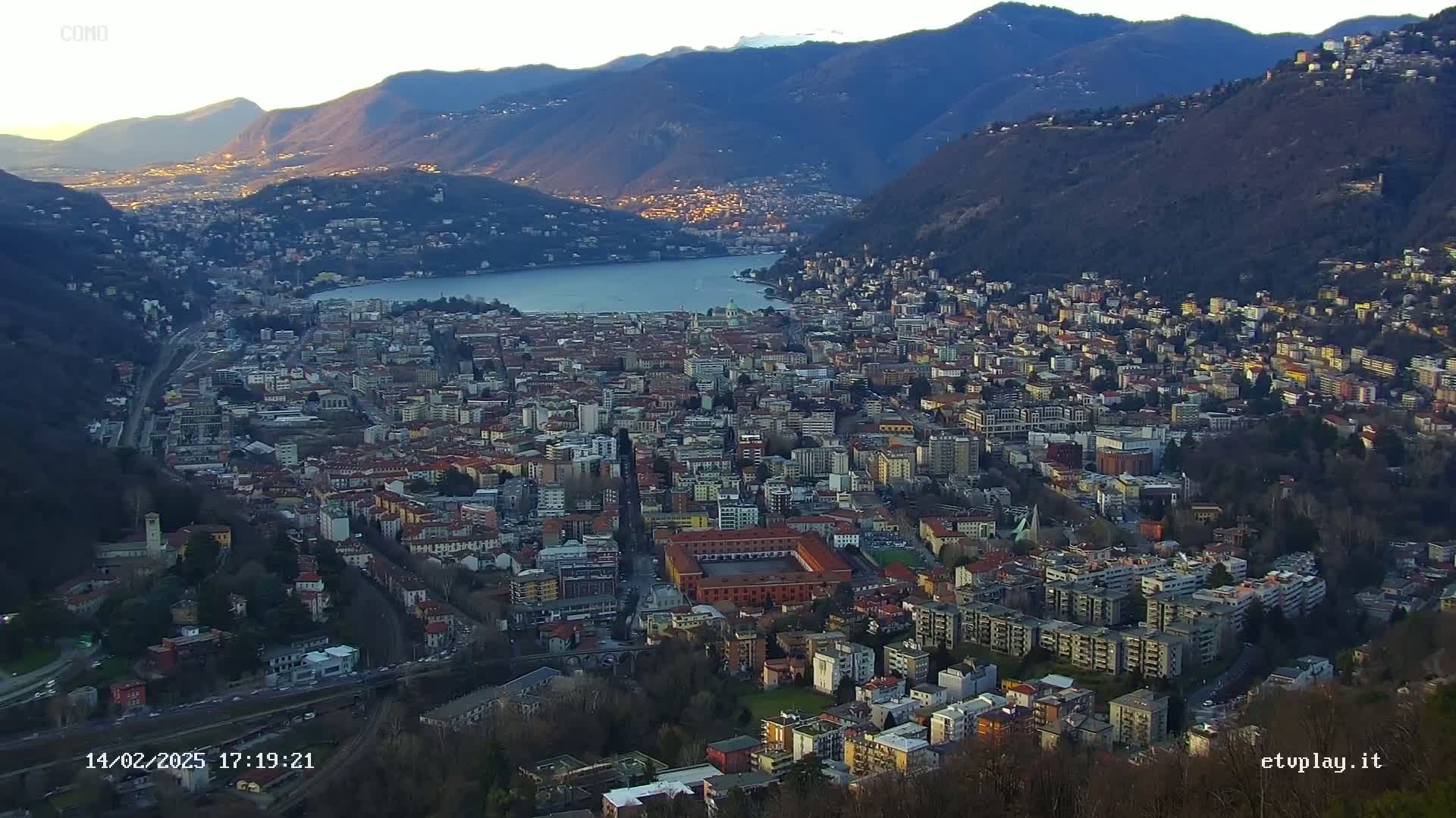 A sprawling city nestled between mountains and a lake under a clear, twilight sky.