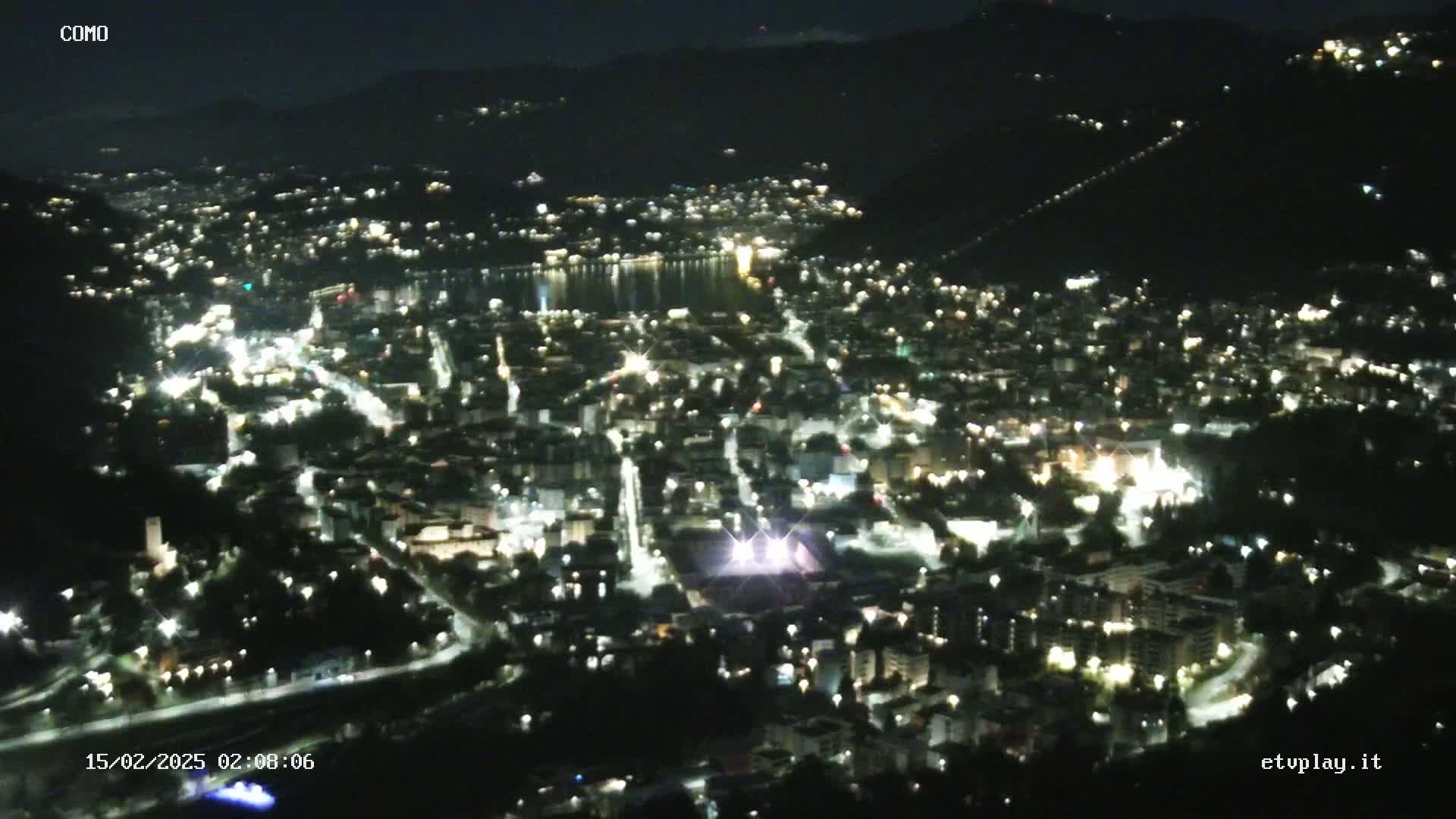 A nighttime, aerial view of a city nestled in a valley, with a body of water visible in the distance.