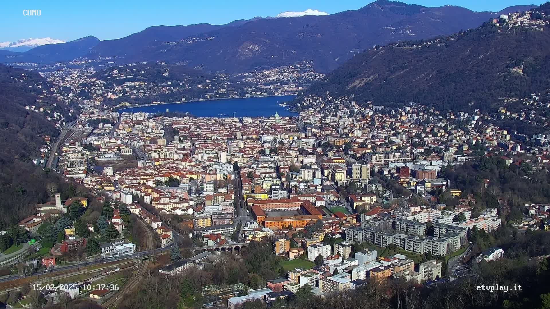 A sprawling city nestled between mountains and a lake under a clear, sunny sky.