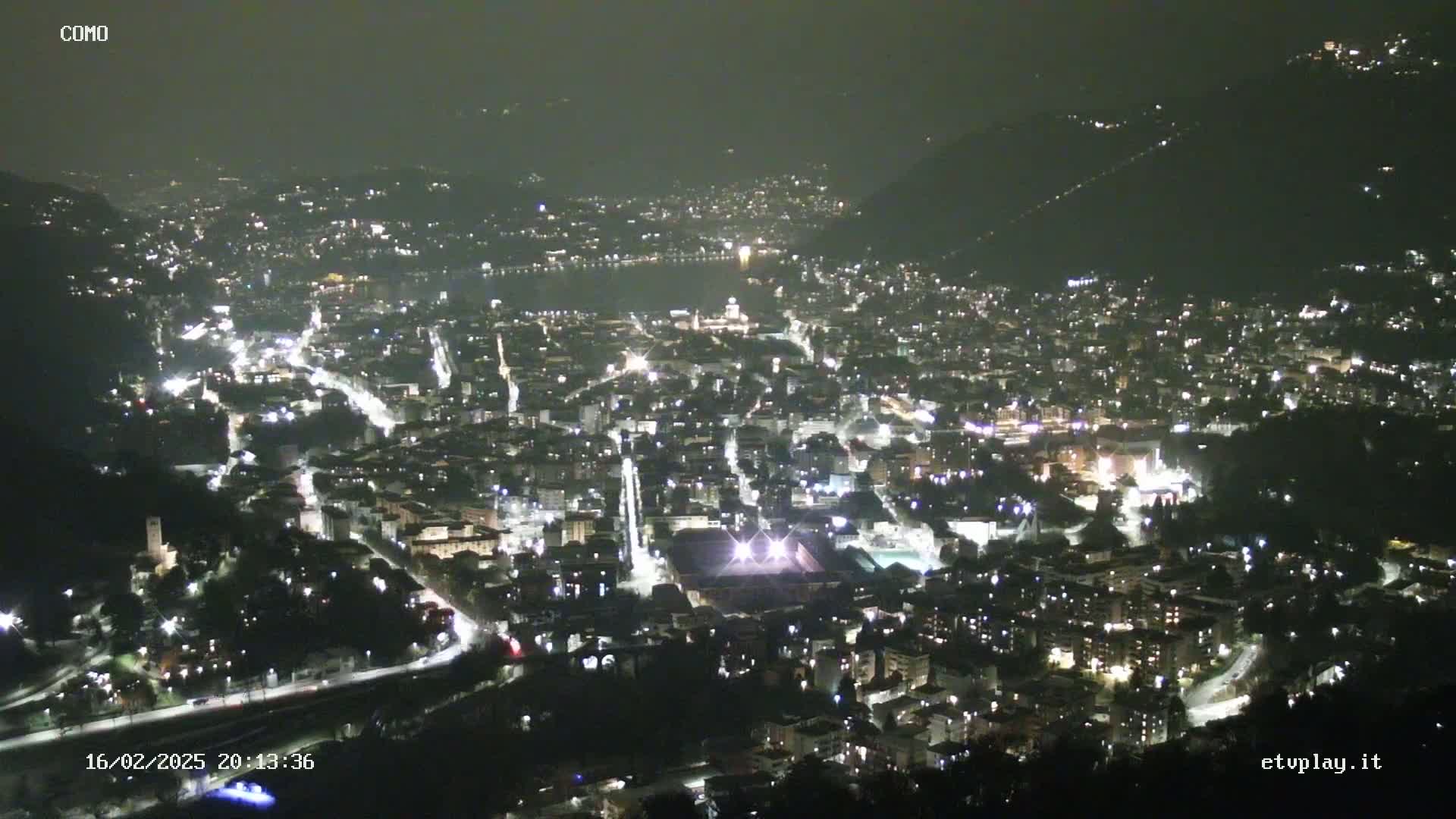 A nighttime aerial view of a city nestled in a valley, illuminated by streetlights and building lights.