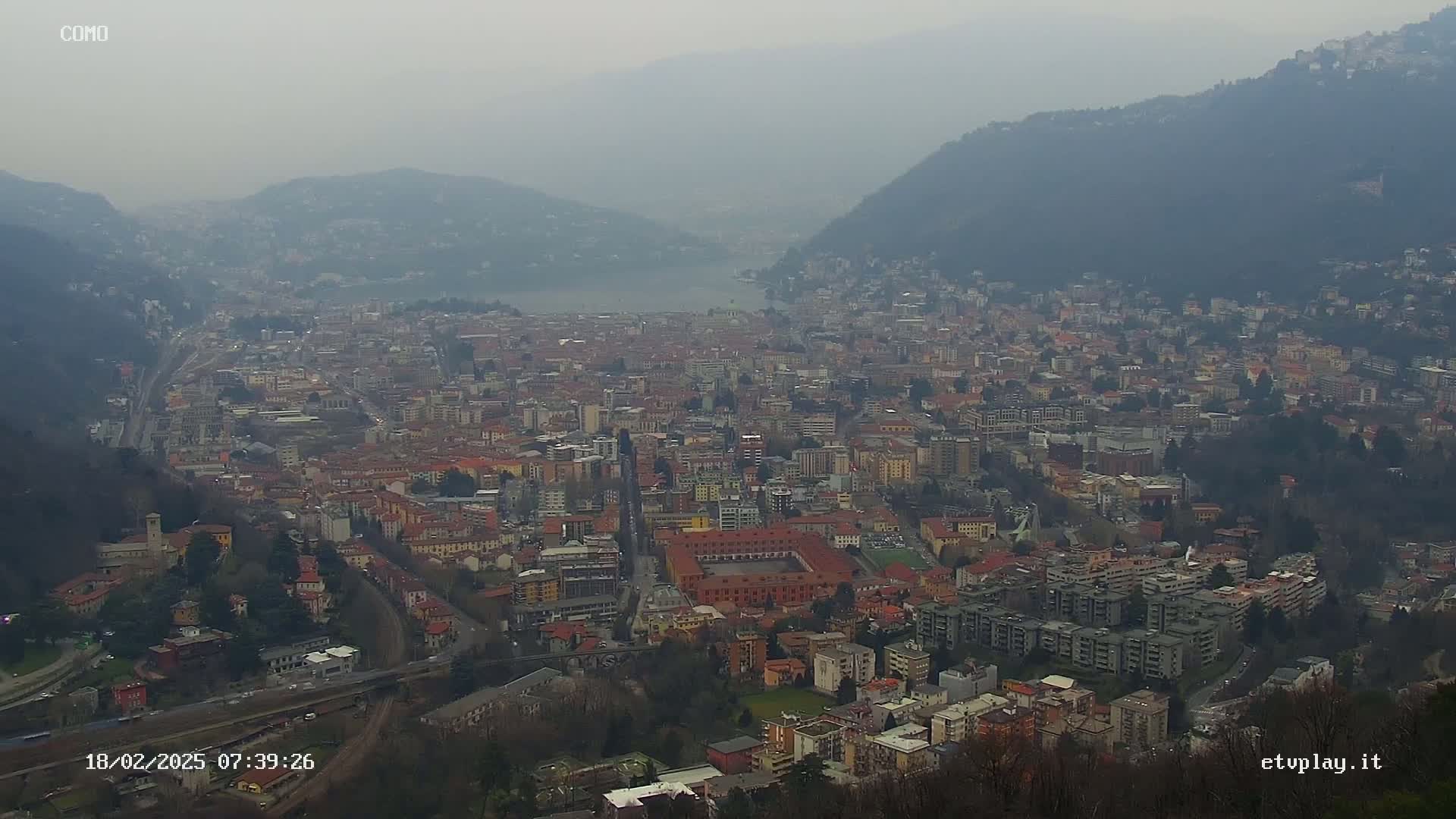 A hazy view shows a sprawling city nestled between mountains, partially obscured by fog or mist.