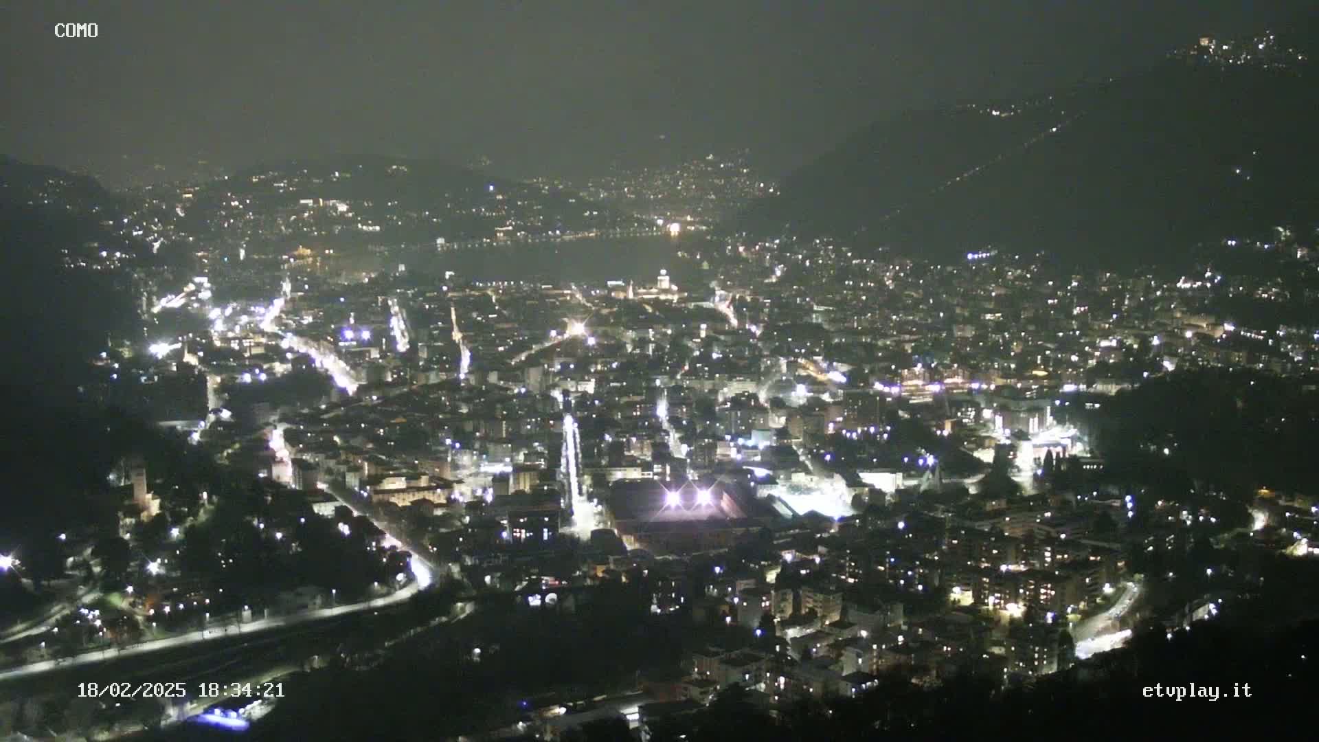 A nighttime, aerial view of a city nestled in a valley, illuminated by numerous lights.