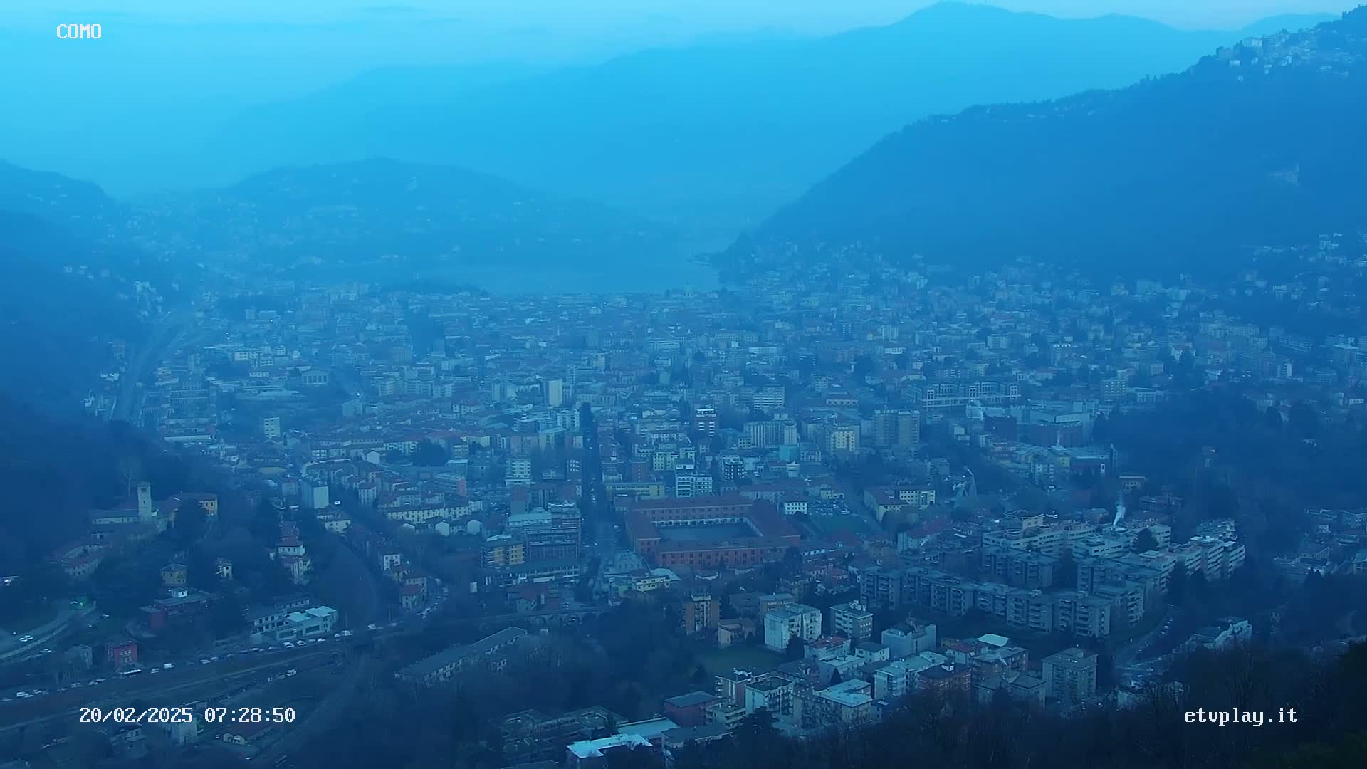 A hazy, twilight view of a sprawling city nestled in a valley between mountains.