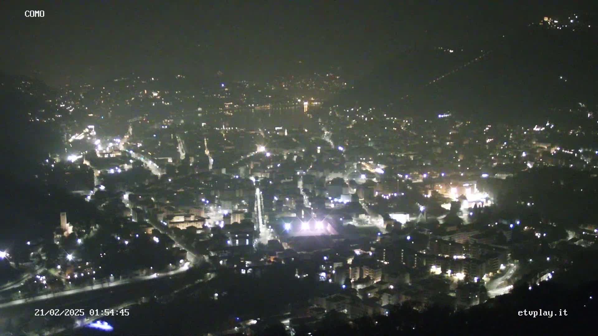 A nighttime, high-angle view of a city illuminated by streetlights, nestled in a valley.
