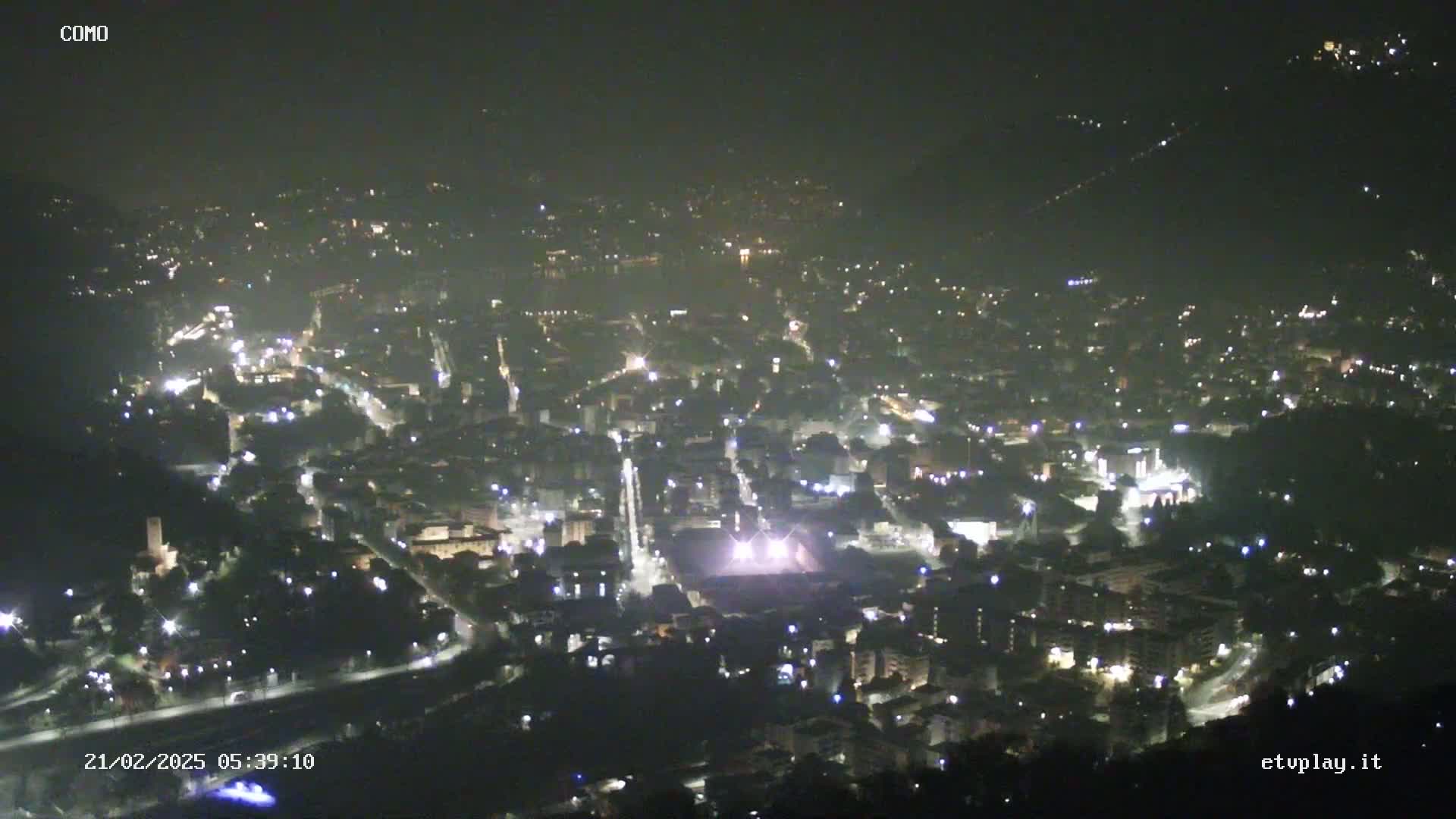 A nighttime, high-angle view of a city illuminated by numerous streetlights, under a dark, clear sky.