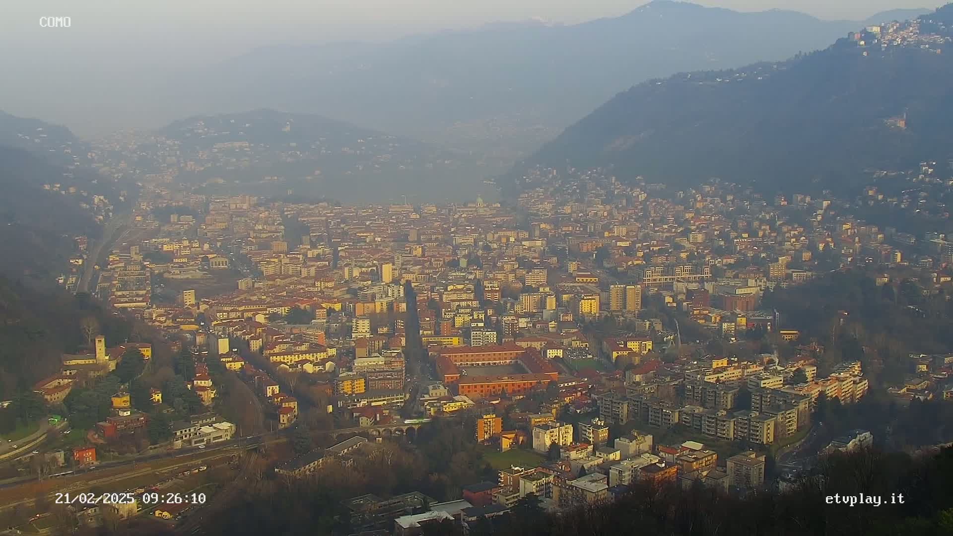 A hazy, high-angle view of a sprawling city nestled in a valley between mountains.