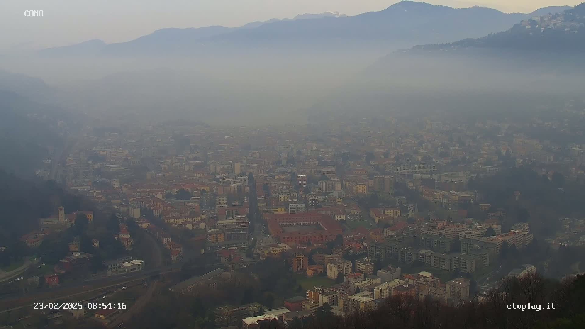 A hazy, foggy view of a sprawling city nestled in a valley between mountains.