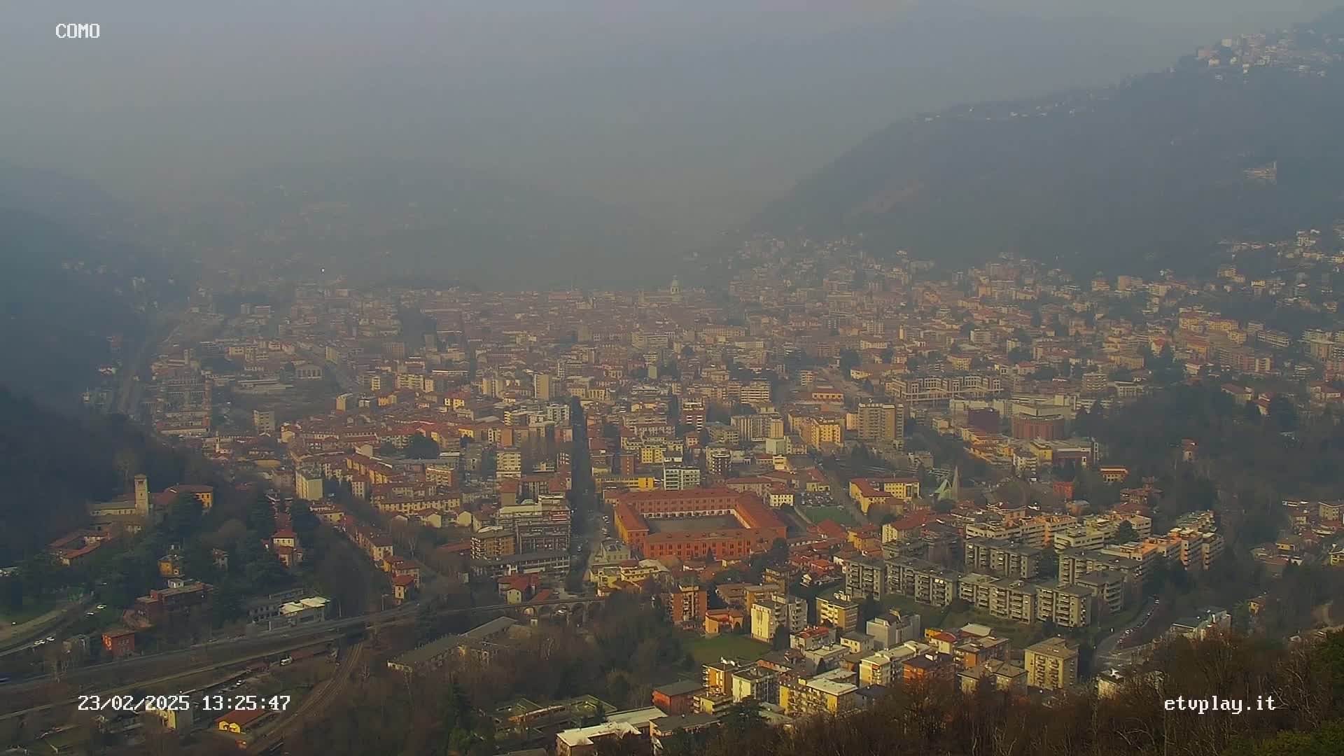 A hazy, distant view of a sprawling city nestled in a valley between hills.
