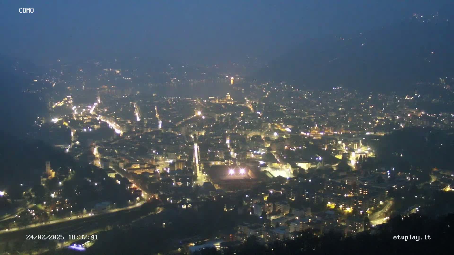 A nighttime, aerial view of a city illuminated by streetlights, under a dark, clear sky.