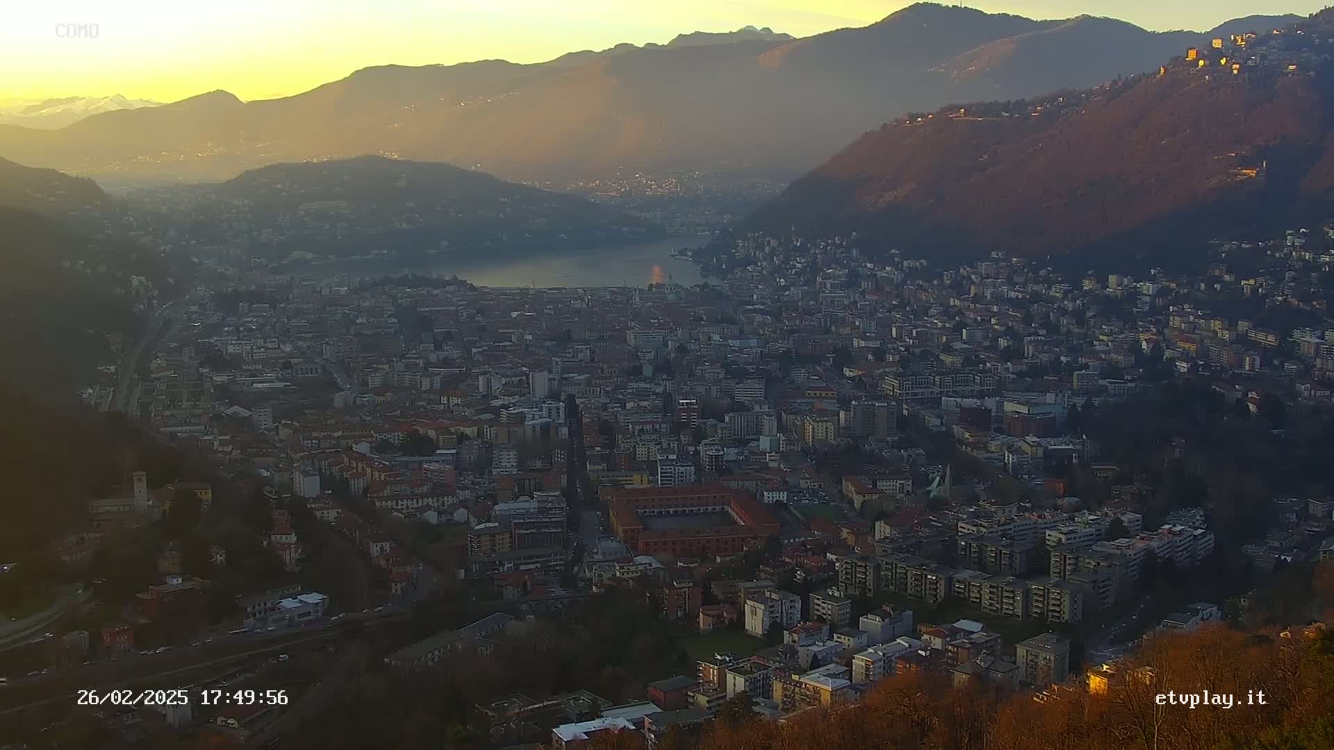 A sprawling city nestled between mountains, overlooking a lake, bathed in the golden light of sunset.