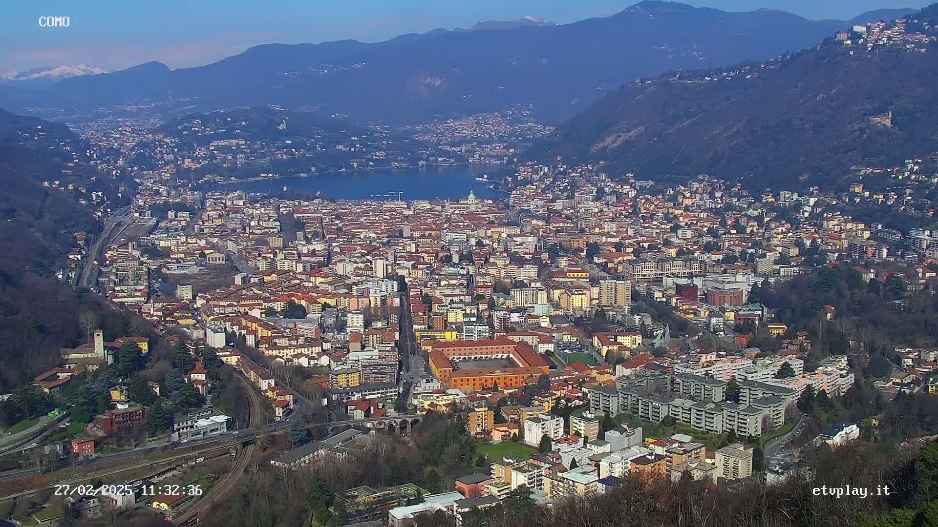 A sprawling city nestled in a valley between mountains, overlooking a lake on a clear, sunny day.