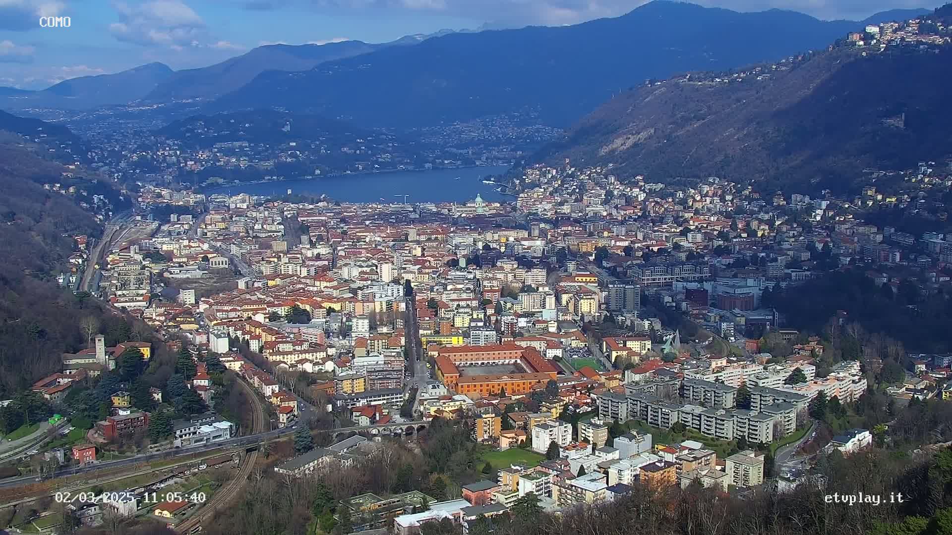 An expansive view of a city nestled between mountains and a lake on a sunny day.