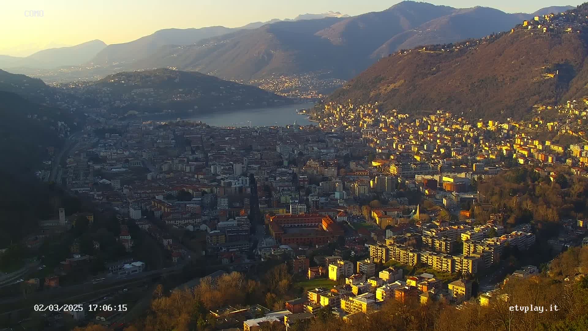 A sprawling city nestled between mountains and a lake at sunset, bathed in the warm glow of the setting sun.