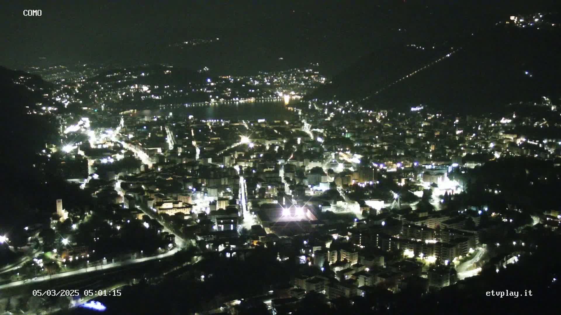 A nighttime, high-angle view of a city illuminated by streetlights, nestled beside a dark body of water.