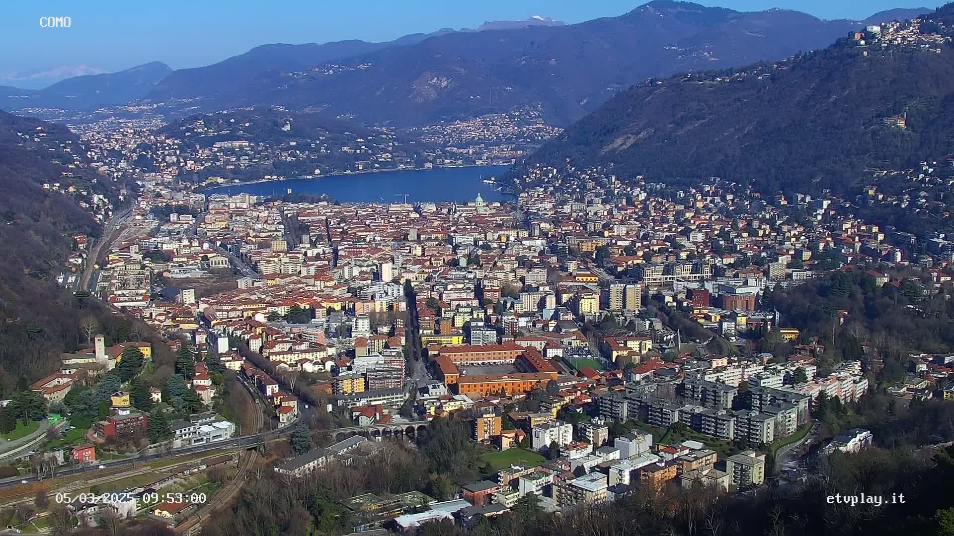 A sprawling city nestled between mountains and a lake on a sunny day.