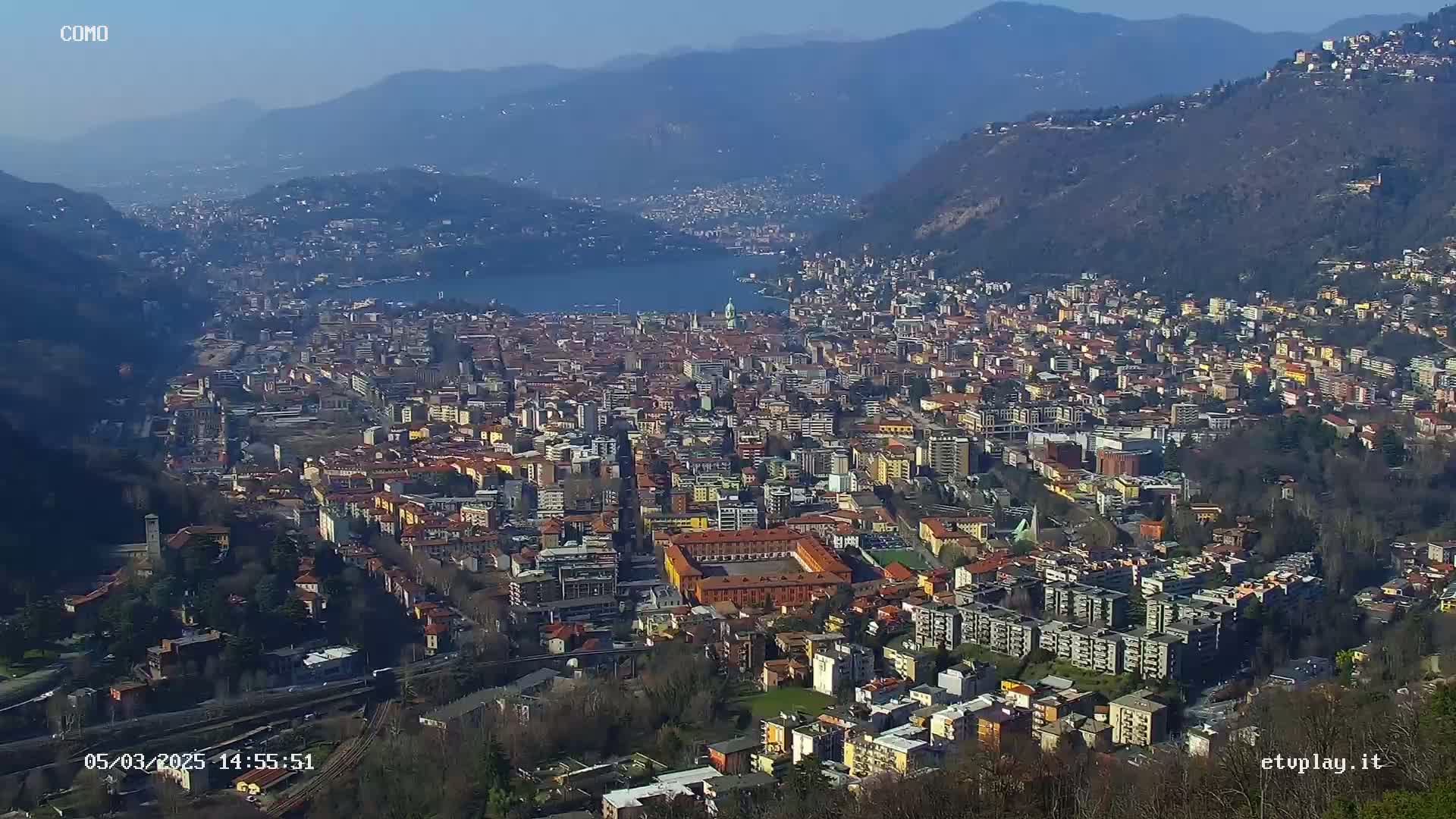 A sprawling city nestled in a valley between mountains, overlooking a lake on a clear, sunny day.