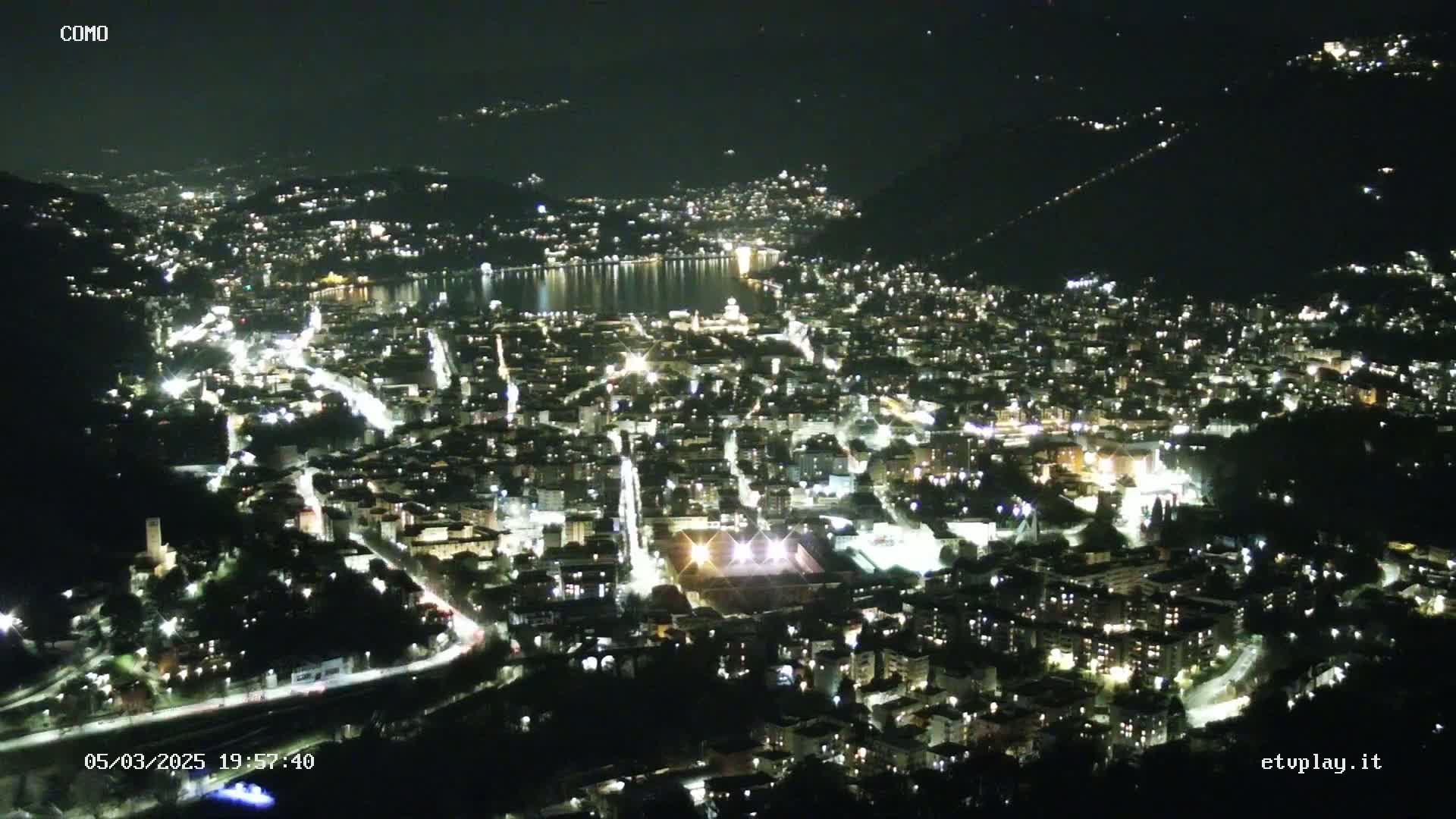 A nighttime, high-angle view of a city illuminated by lights, nestled beside a body of dark water.