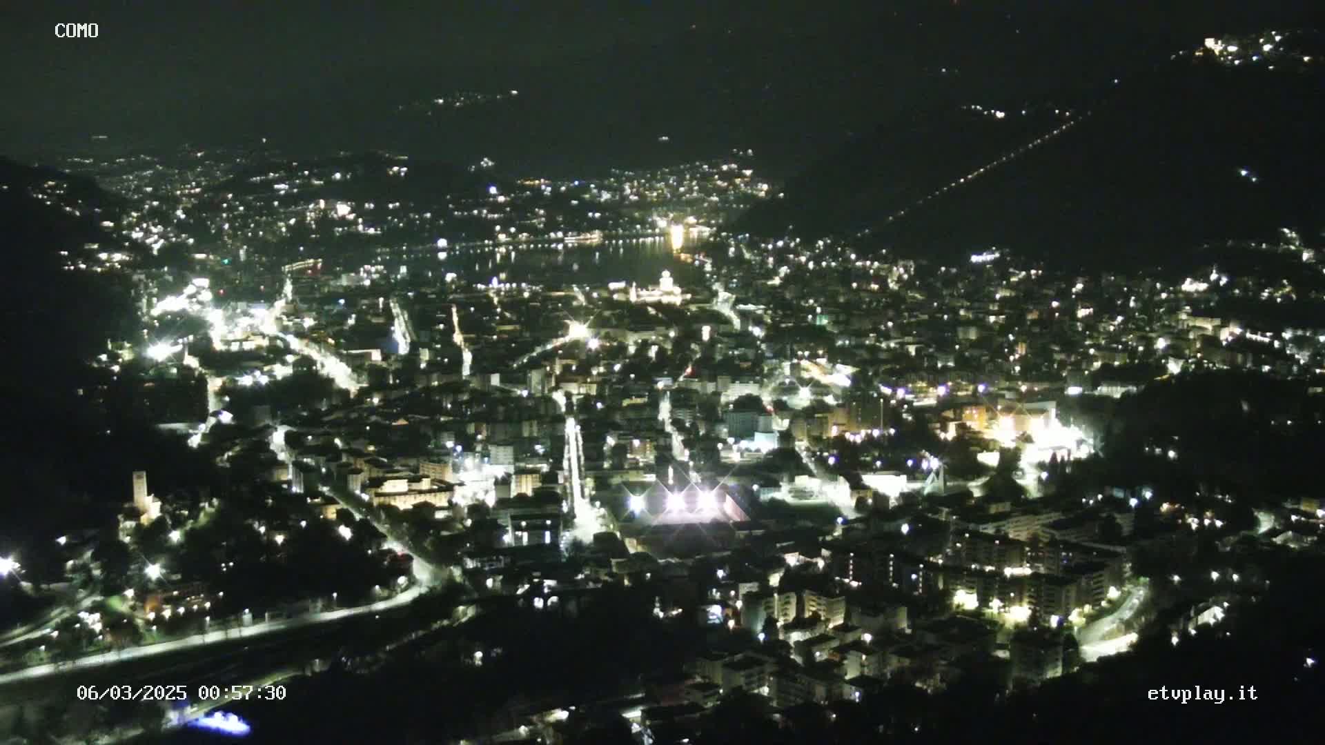 A nighttime, high-angle view of a city illuminated by lights, situated near a body of water.