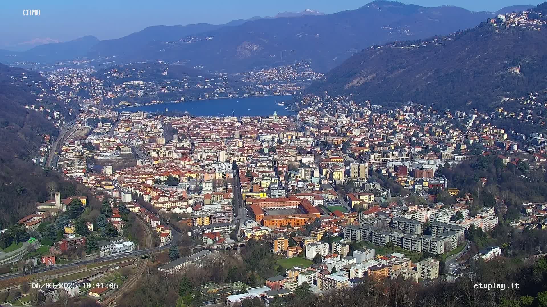 A sprawling city nestled in a valley between mountains, overlooks a lake on a clear, sunny day.
