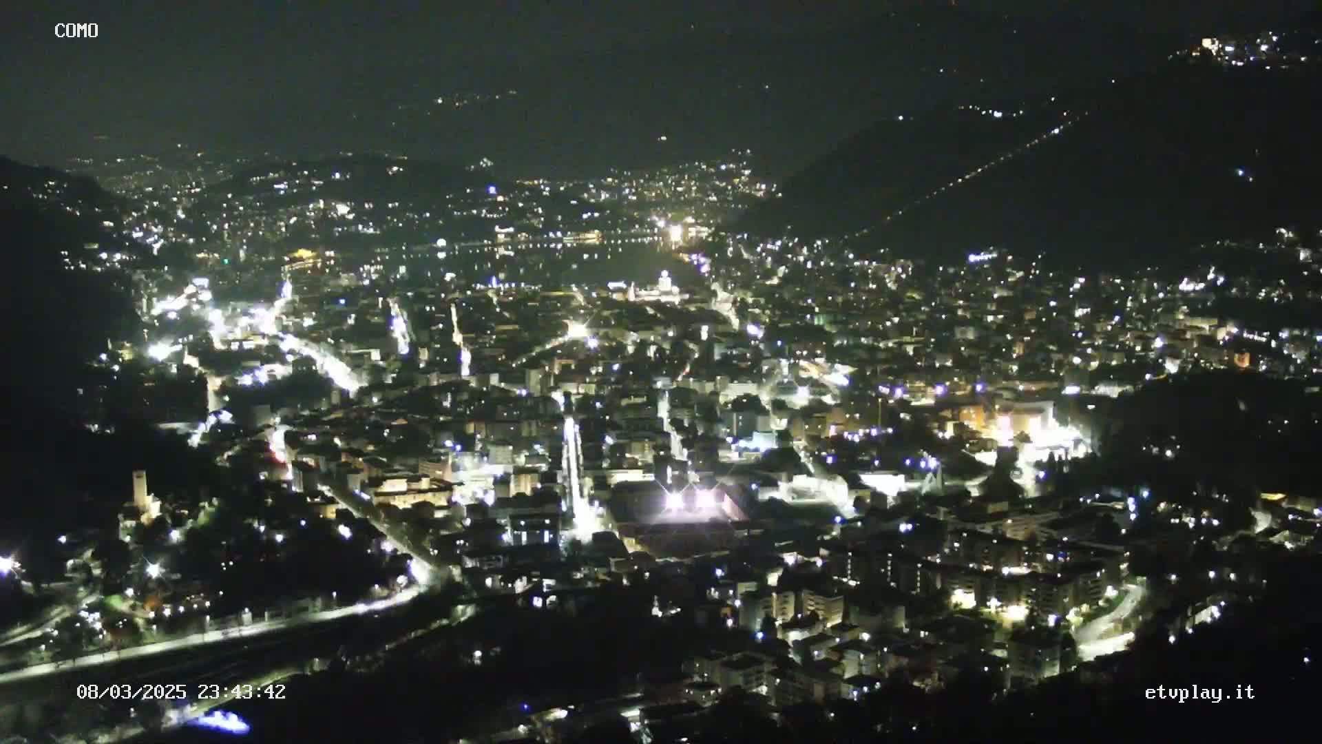 A nighttime, aerial view of a city nestled in a valley, illuminated by numerous lights.