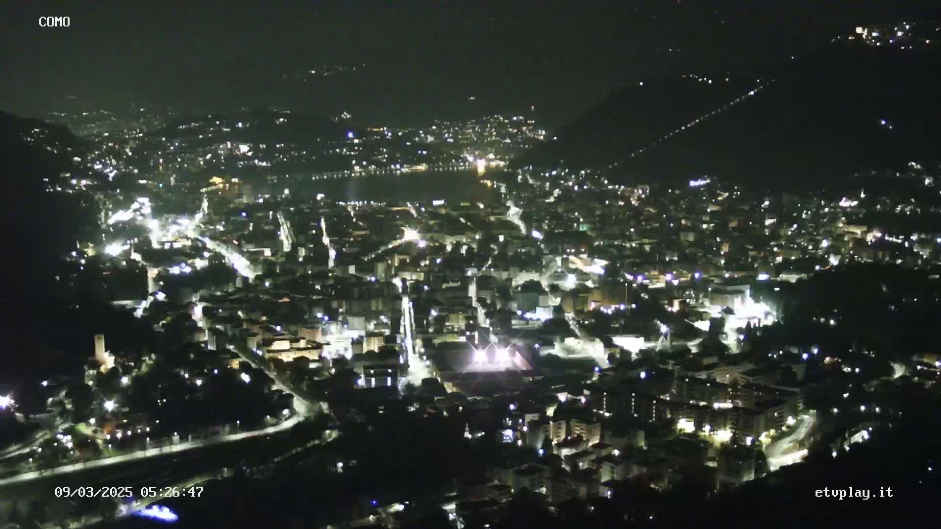 A nighttime aerial view of a city nestled in a valley, illuminated by numerous lights.