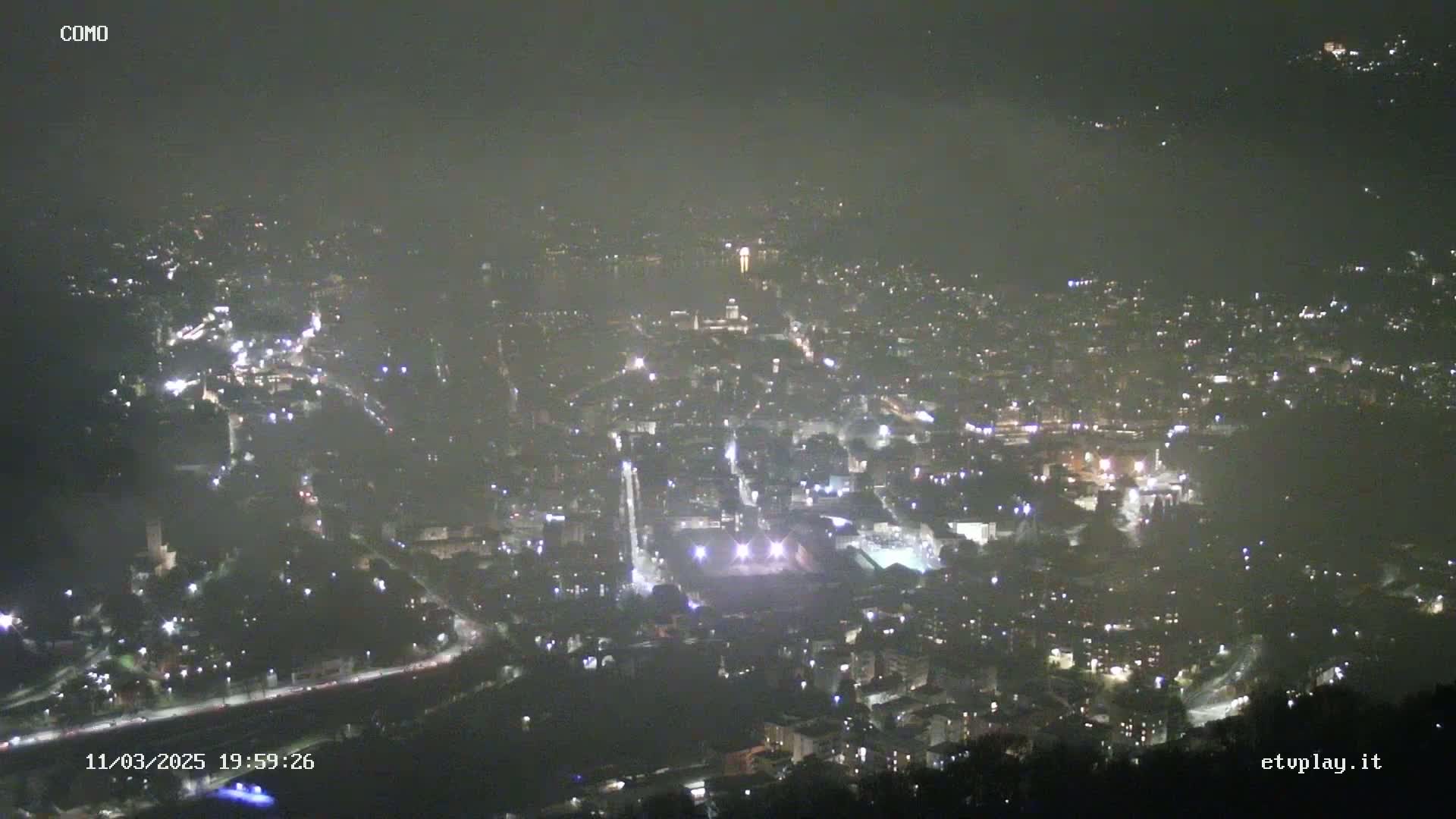 A nighttime, hazy view of a city illuminated by numerous lights, seen from a high vantage point.