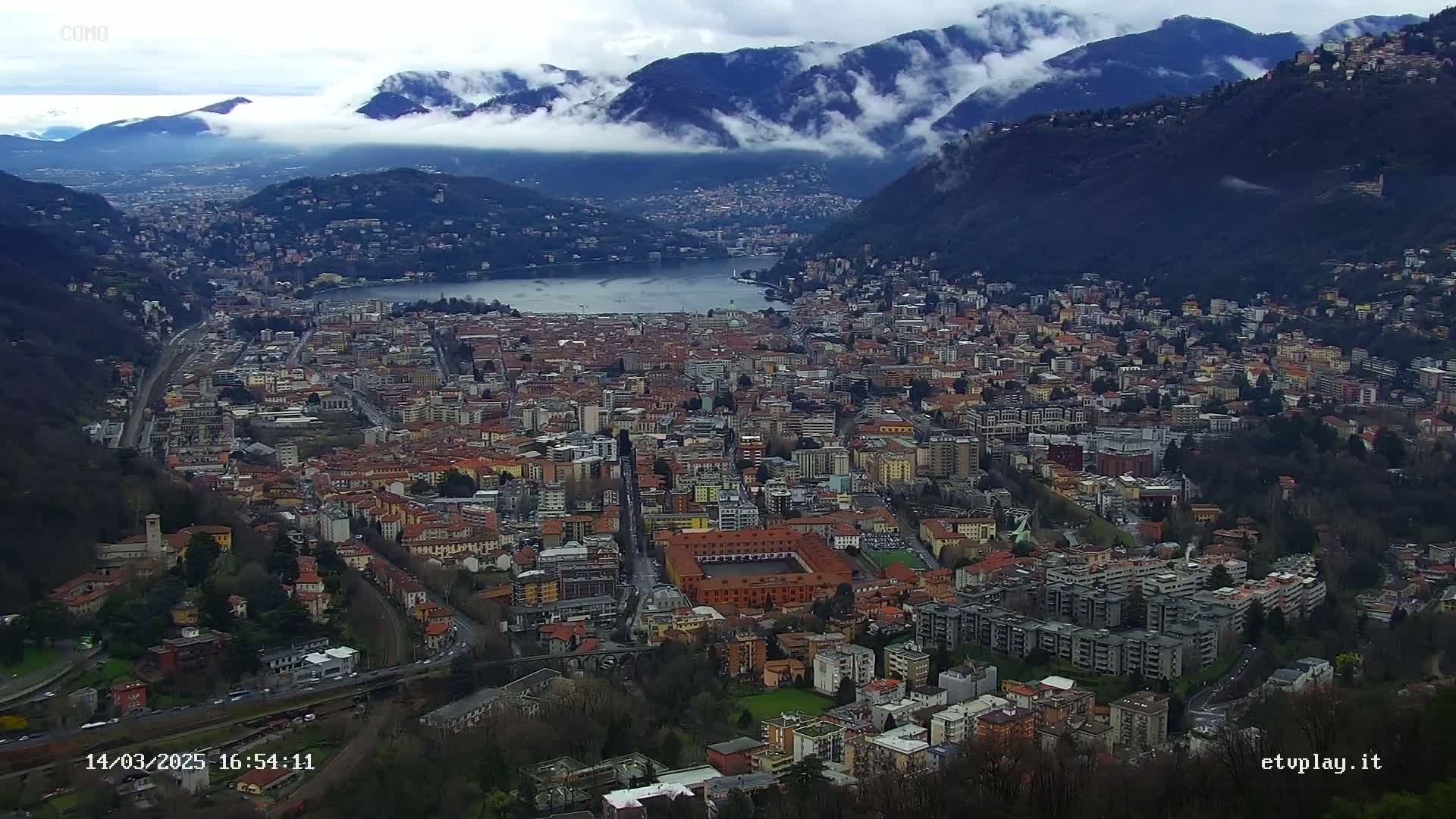 A sprawling city nestled in a valley between mountains, partially obscured by low-hanging clouds.