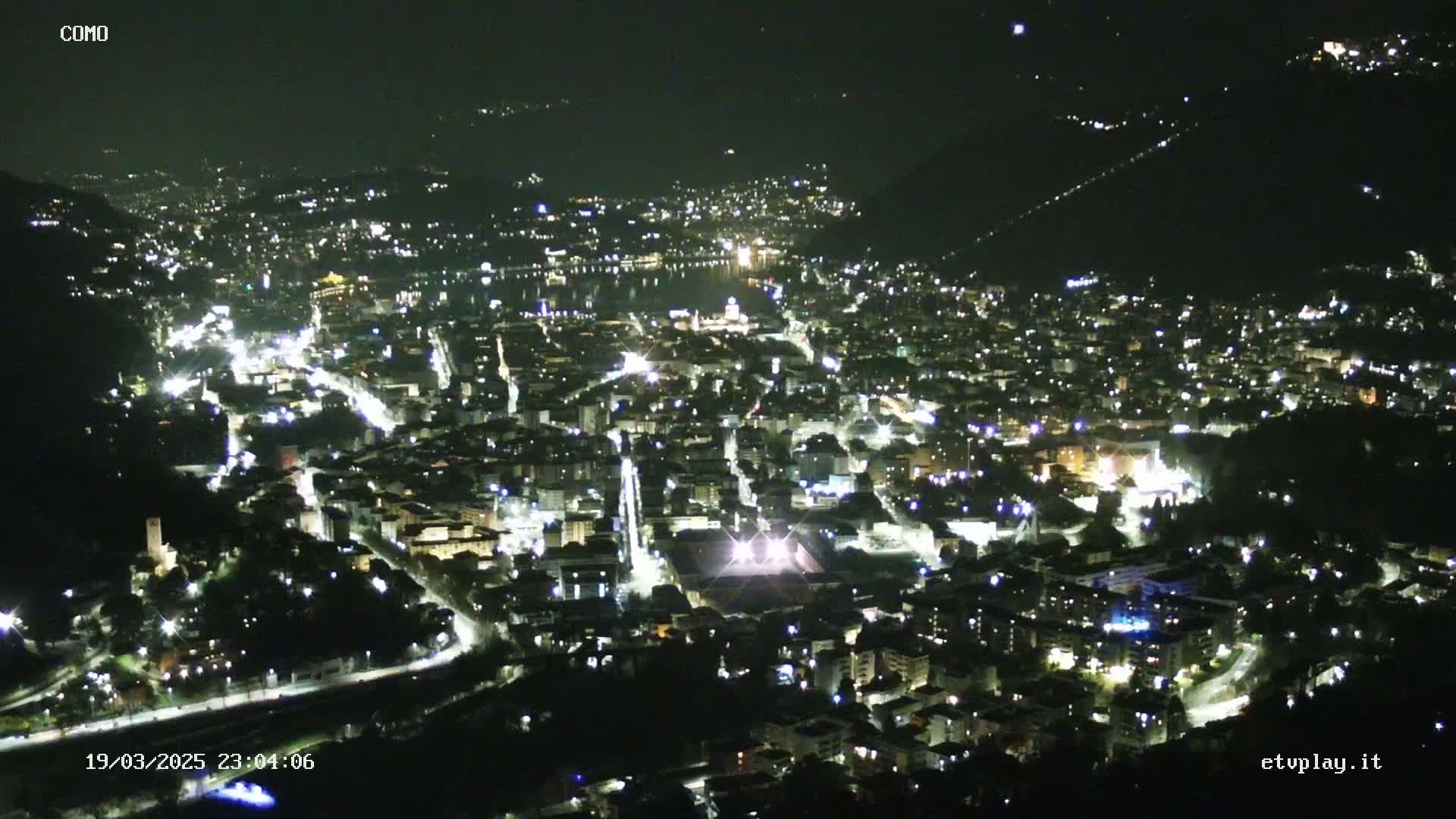 A nighttime, aerial view of a city nestled in a valley, illuminated by numerous streetlights.