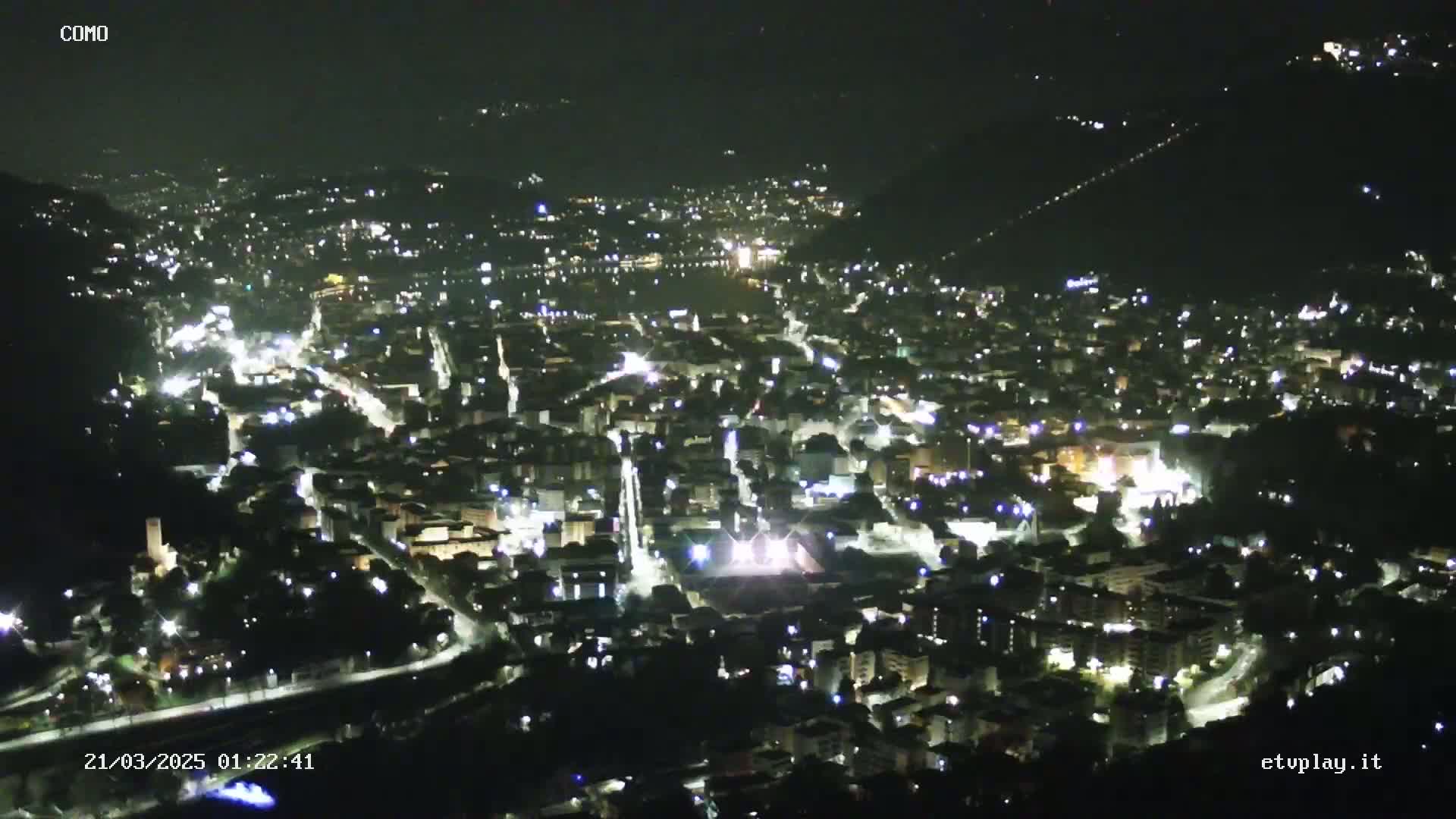 A nighttime aerial view of a city nestled in a valley, illuminated by numerous streetlights.