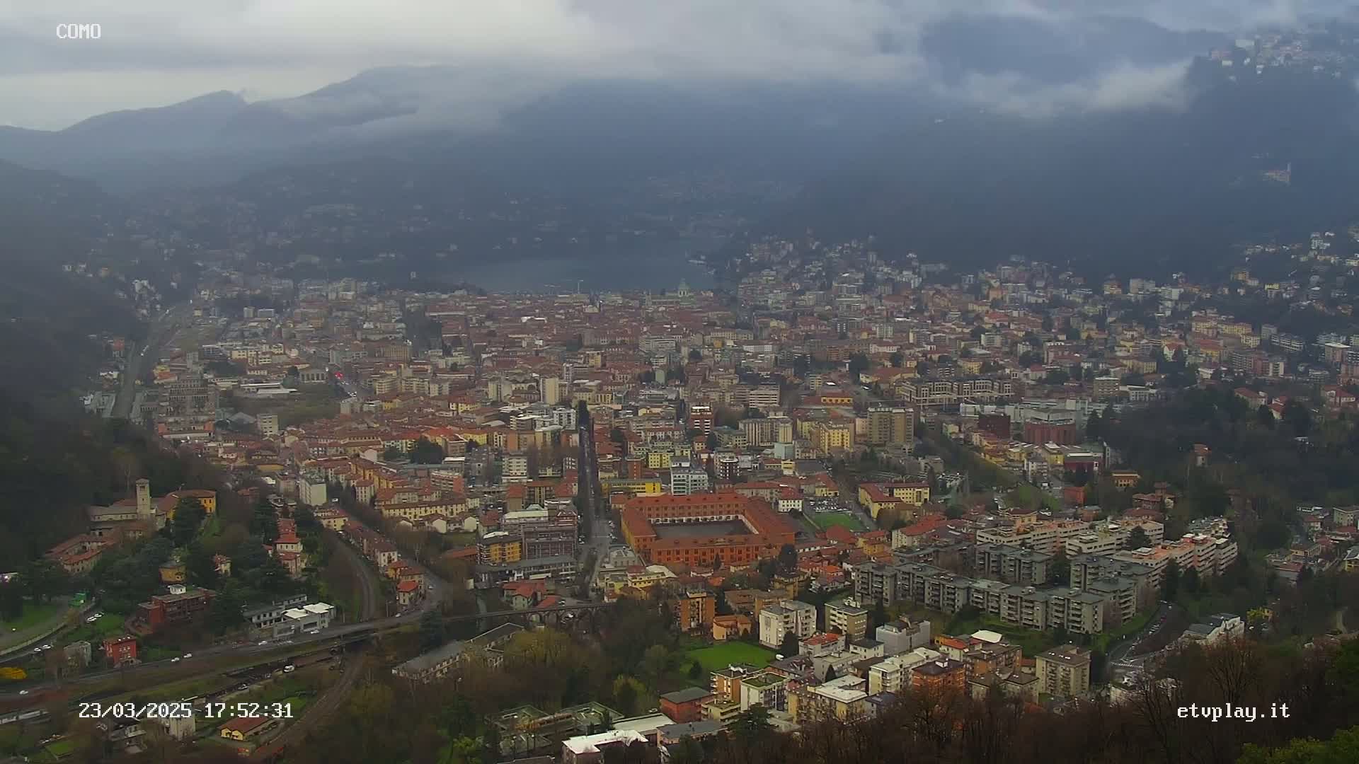A sprawling city nestled in a valley between mountains under a cloudy sky.