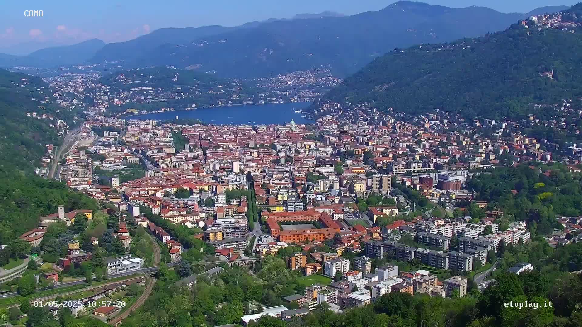 A sprawling city nestled between mountains and a lake under a clear, sunny sky.