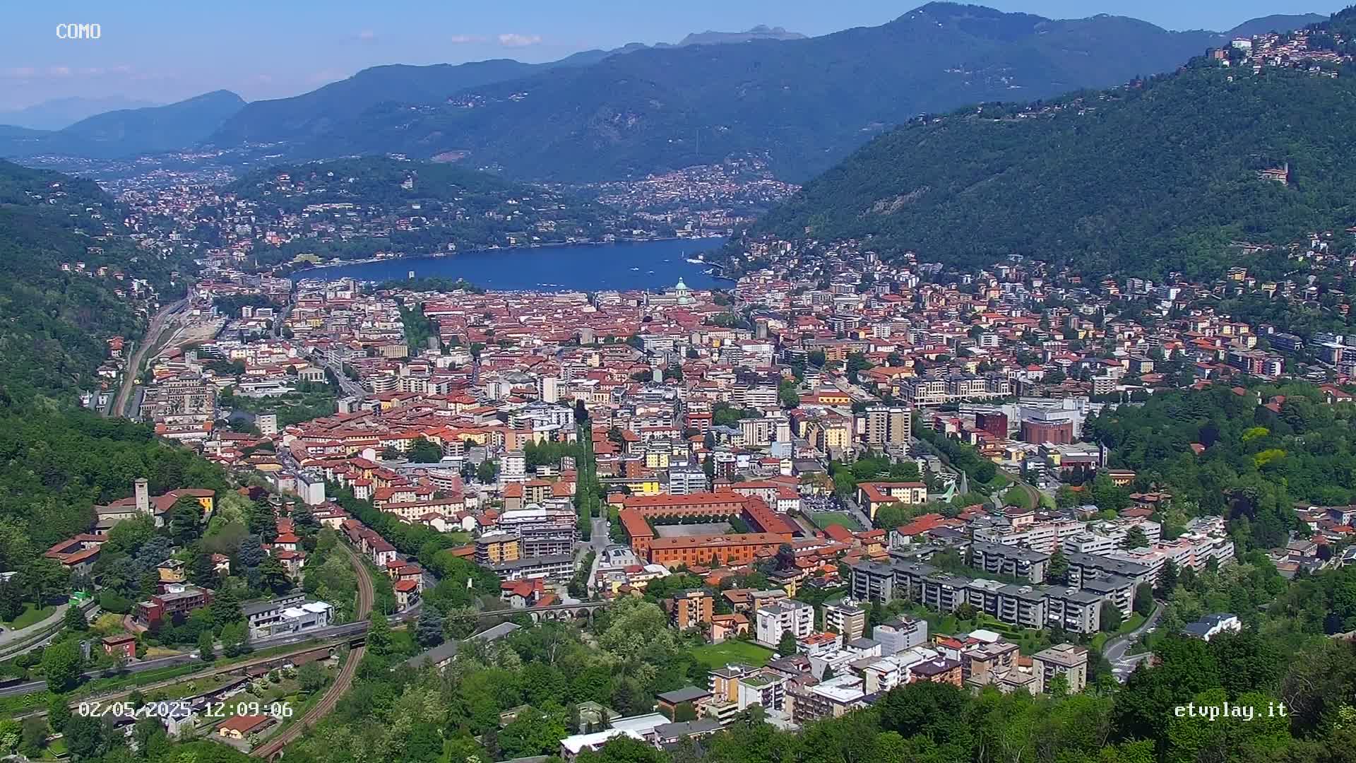 A sprawling city nestled in a valley between mountains, overlooking a calm lake under a clear sky.