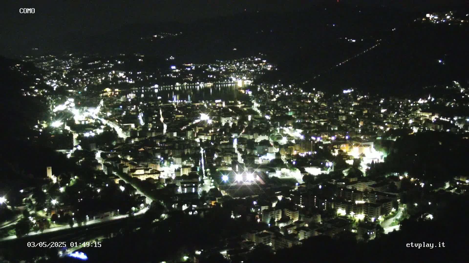 A nighttime, high-angle view of a city illuminated by lights, situated near a body of water.