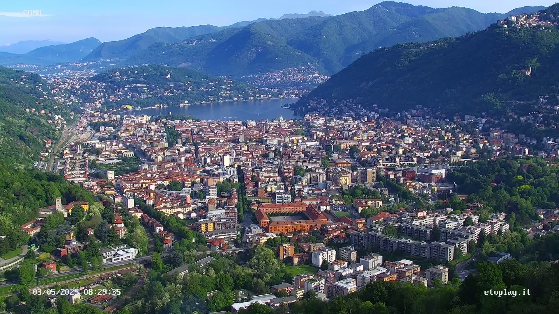 A sprawling city nestled in a valley between mountains, overlooks a lake under a clear blue sky.