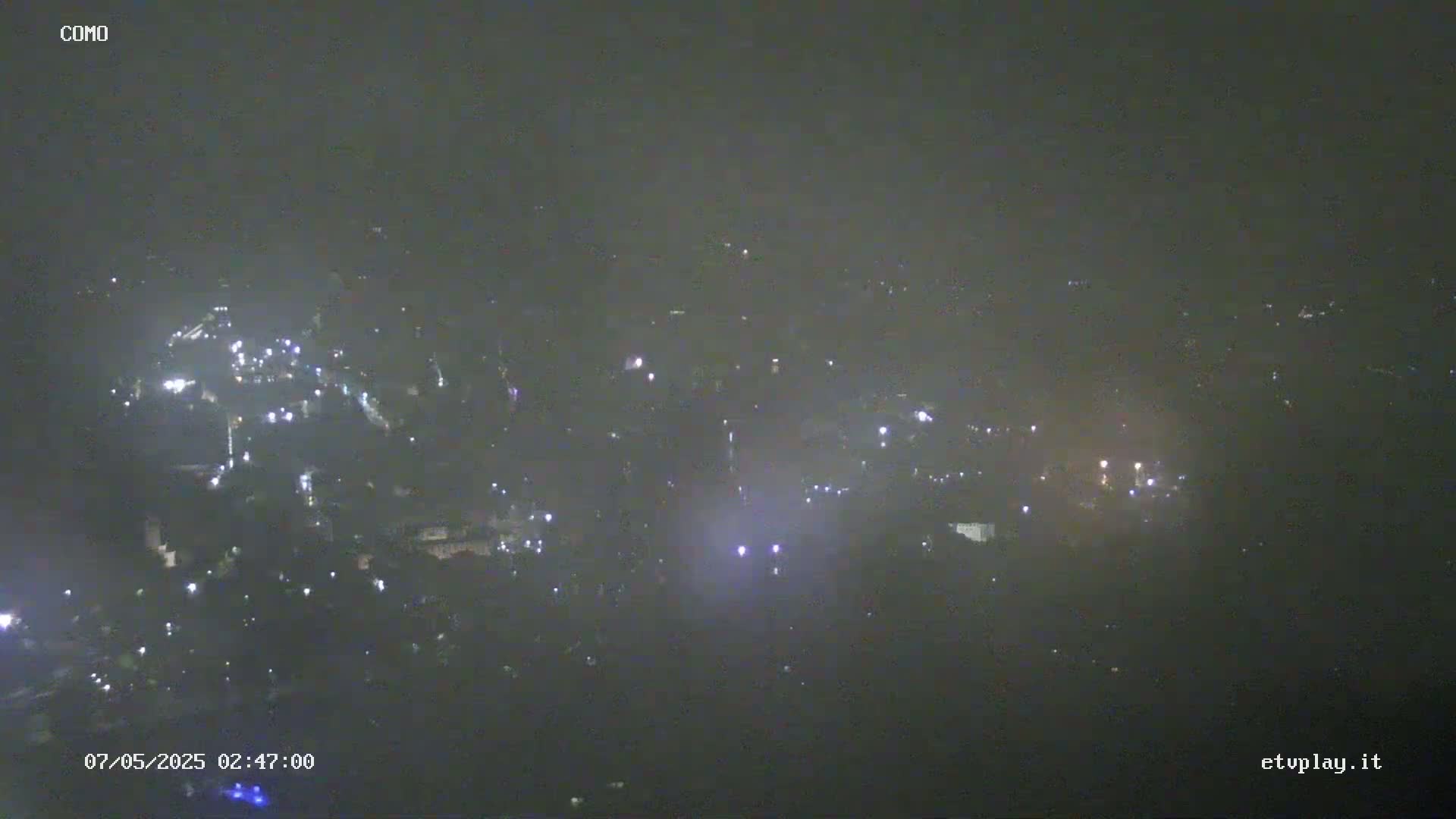 A hazy night view shows a scattering of lights from a distant town or city.