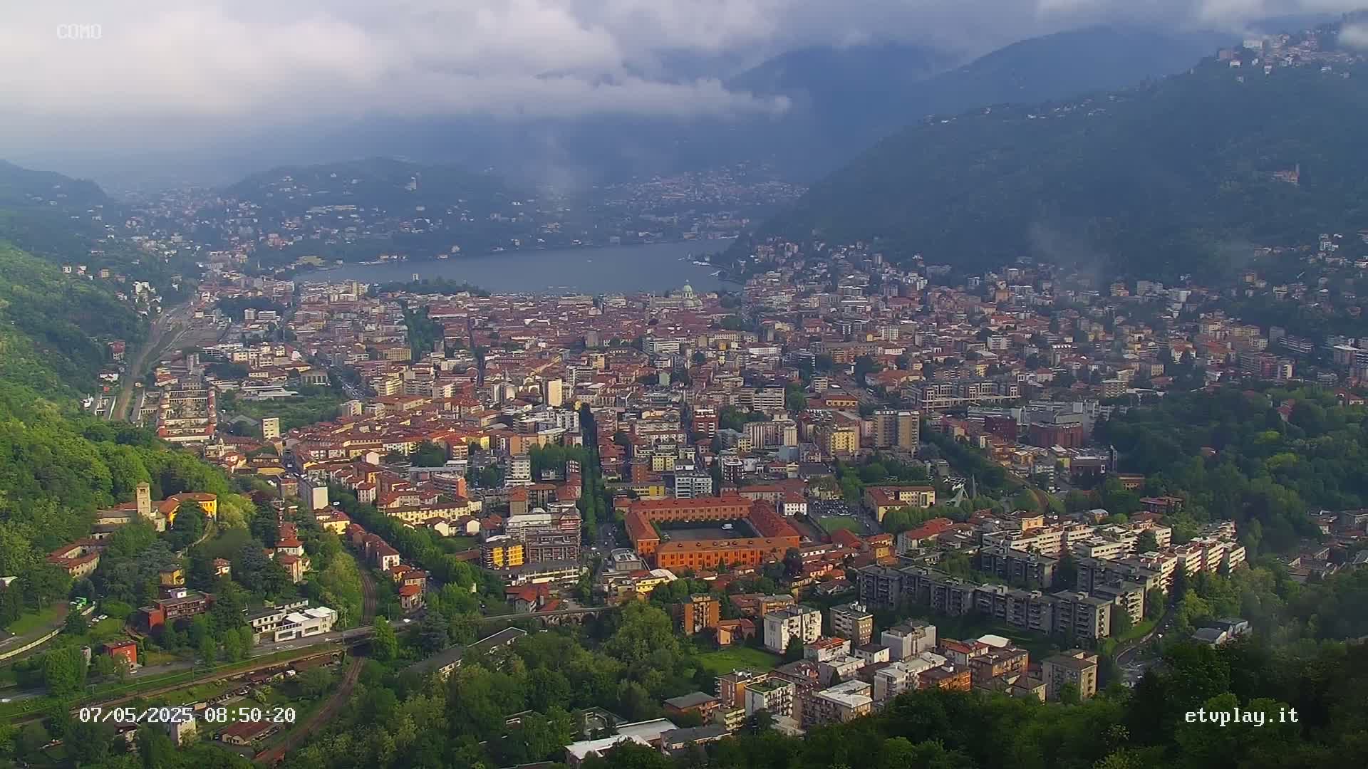 An expansive city nestled between hills and a lake under a cloudy sky.