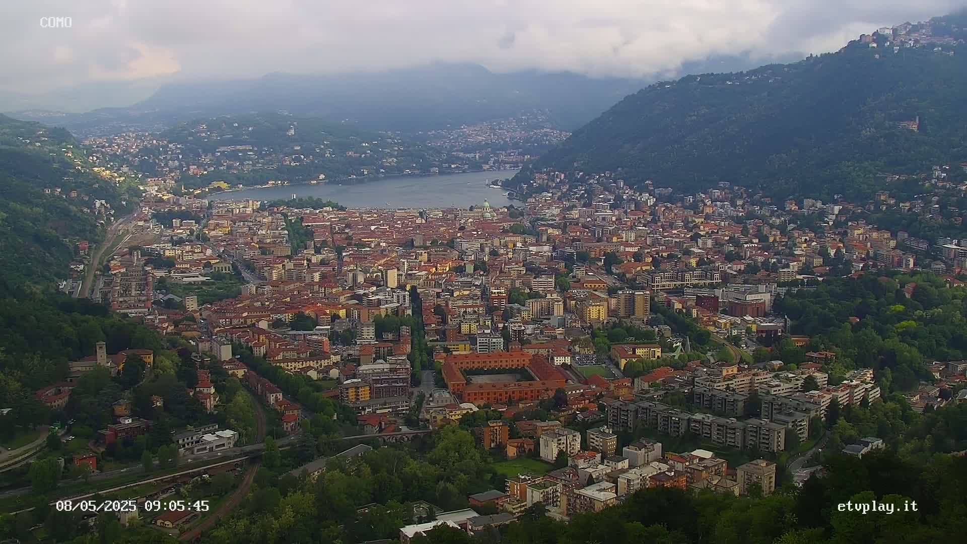 An expansive city nestled between a lake and mountains under an overcast sky.