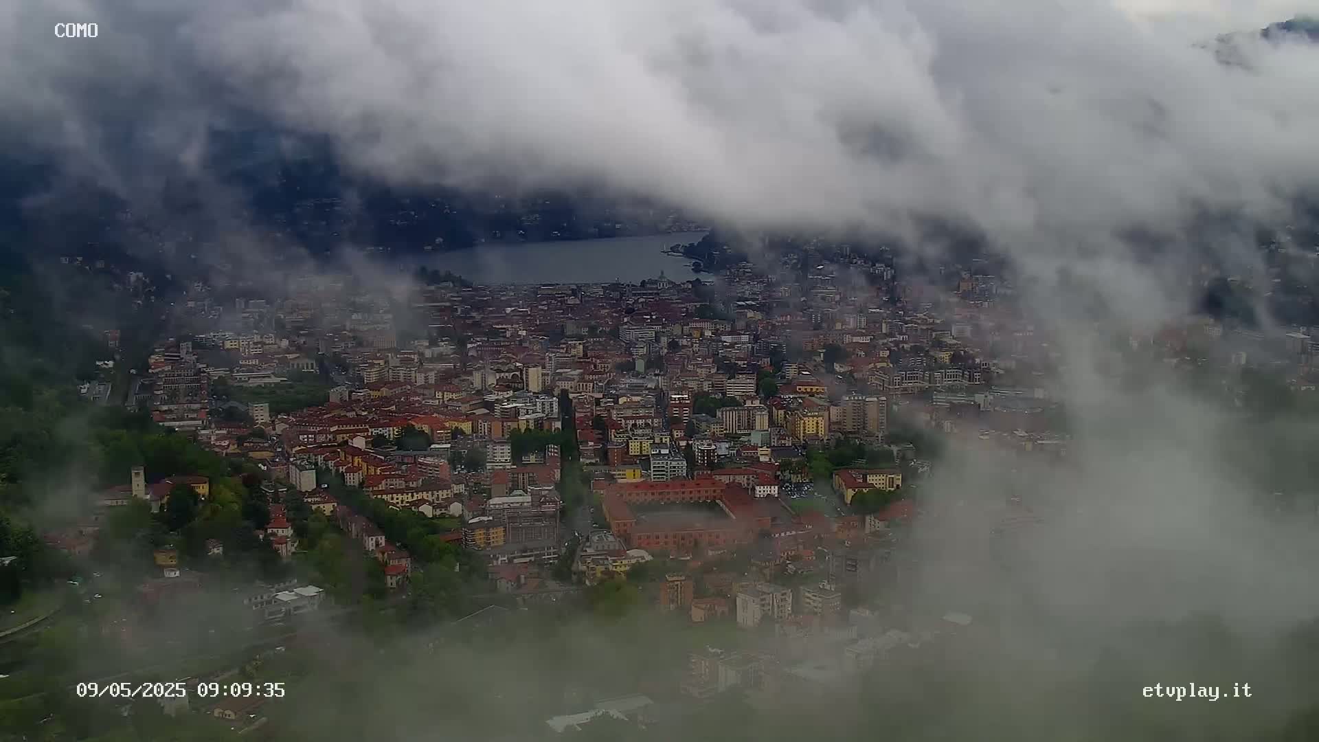 A city nestled beside a lake is partially obscured by a thick fog.