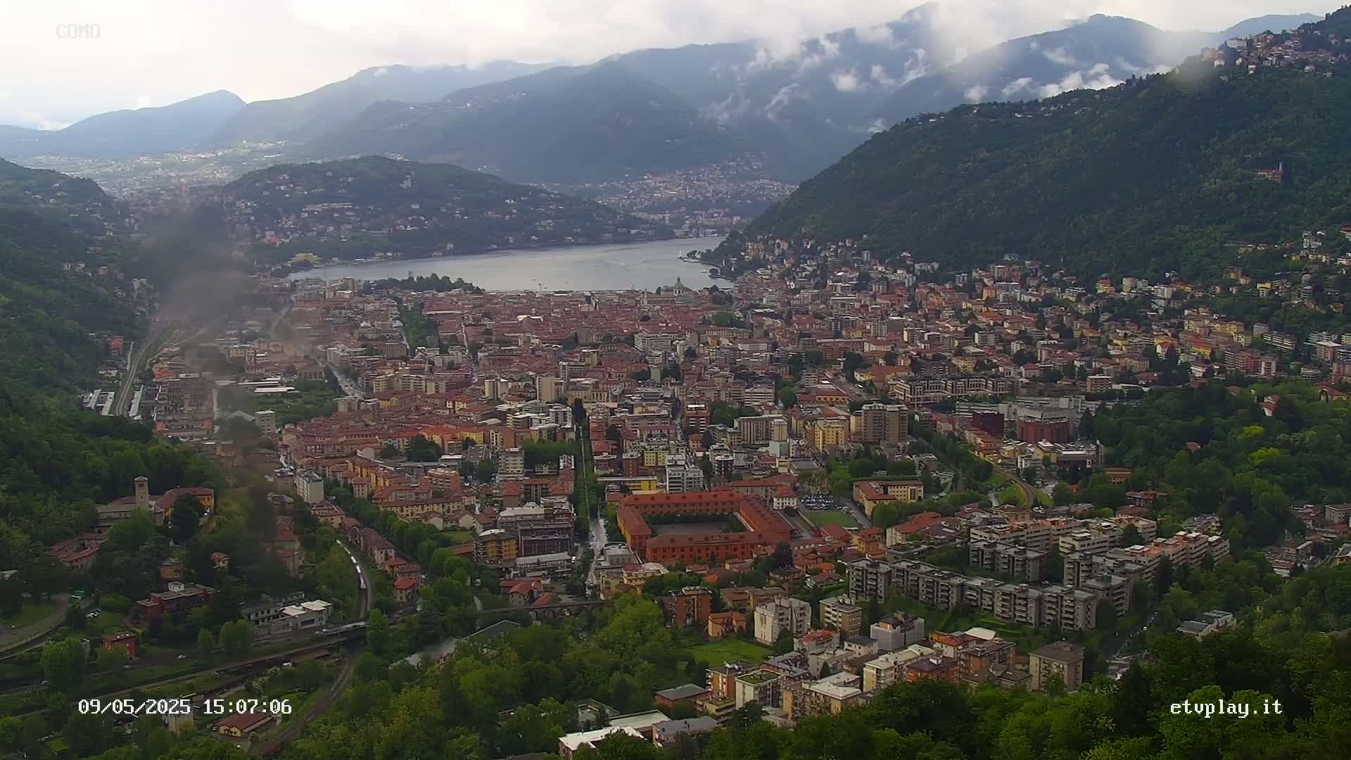 A sprawling city nestled between mountains and a lake under an overcast sky.