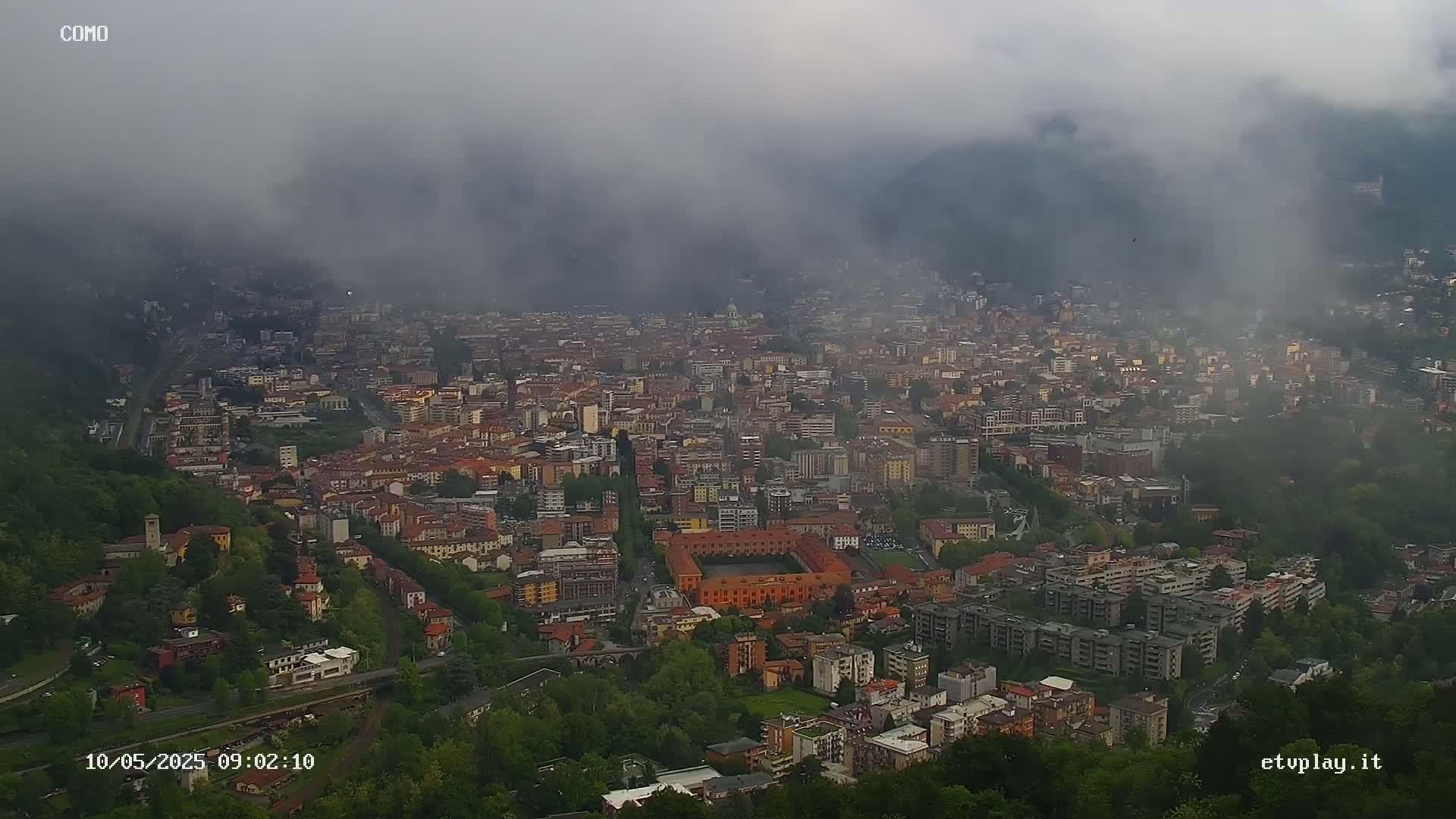 A foggy view of a densely populated city nestled in a valley, surrounded by lush green hills.