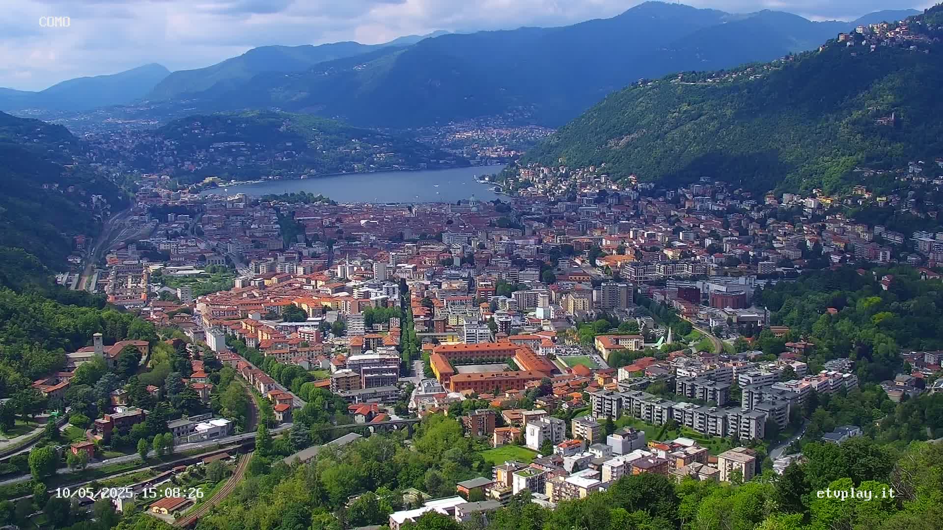 A sprawling city nestled between a lake and mountains under a partly cloudy sky.