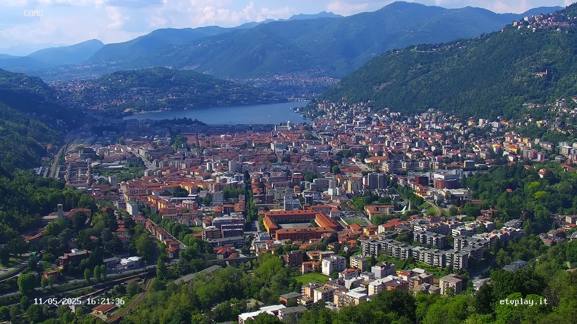 A sprawling city nestled in a valley between mountains, alongside a calm lake under a clear blue sky.