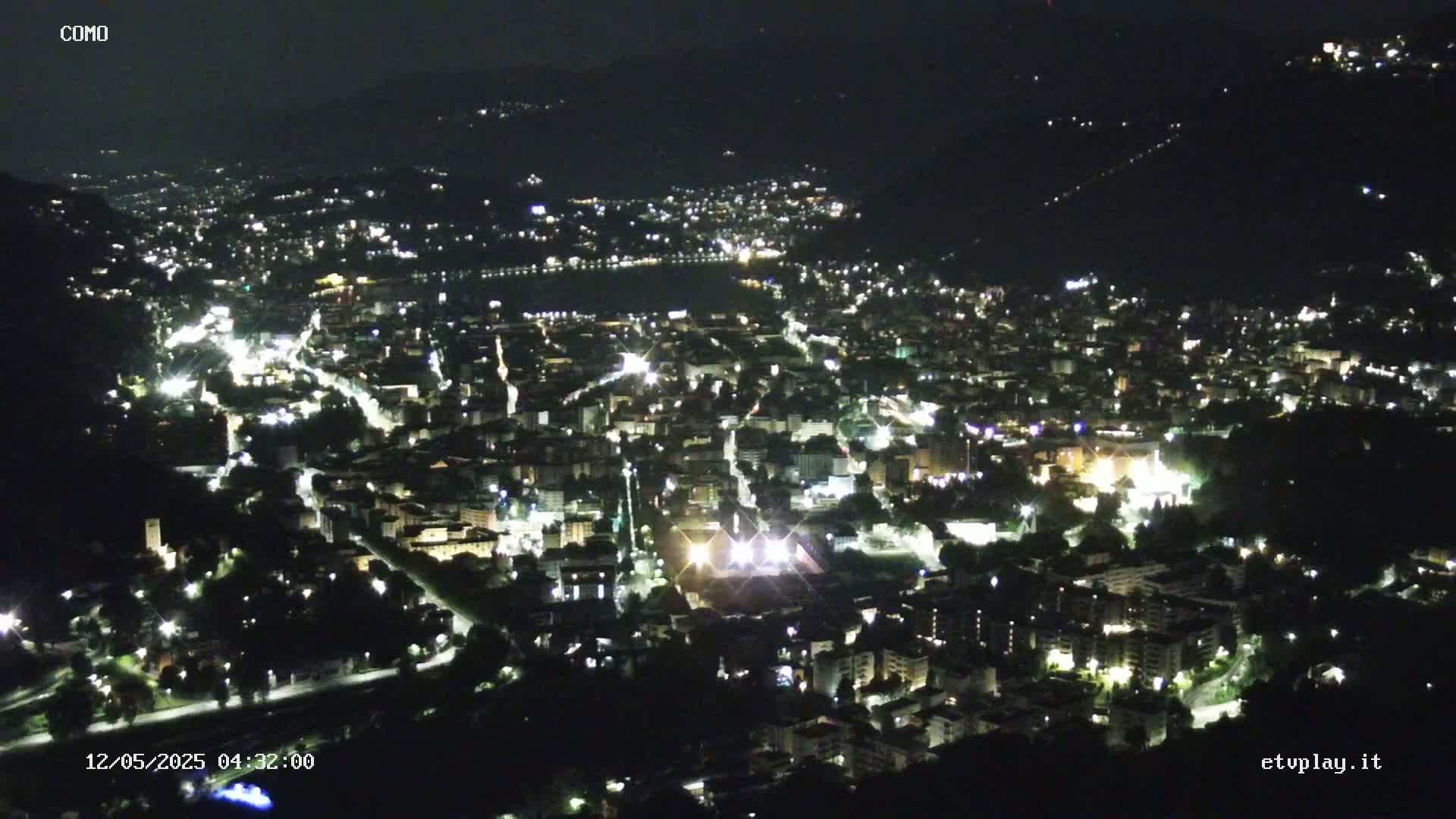 A nighttime, high-angle view of a city illuminated by streetlights and building lights, nestled within a valley.