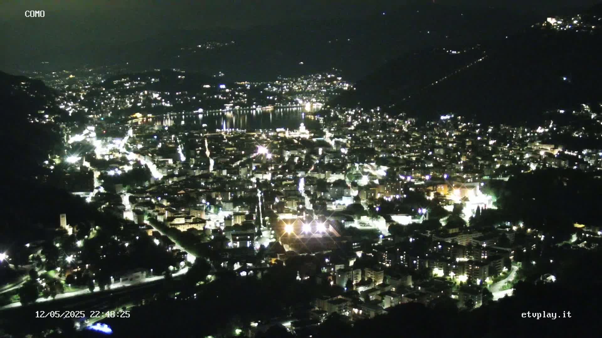 A nighttime, high-angle view of a city illuminated by lights, situated beside a body of water nestled in a valley.