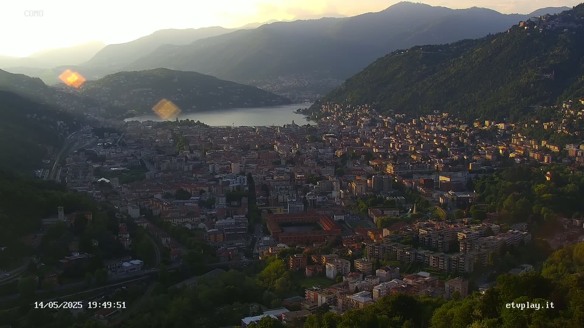 An expansive view of a city nestled in a valley at sunset, overlooking a lake and surrounded by mountains.