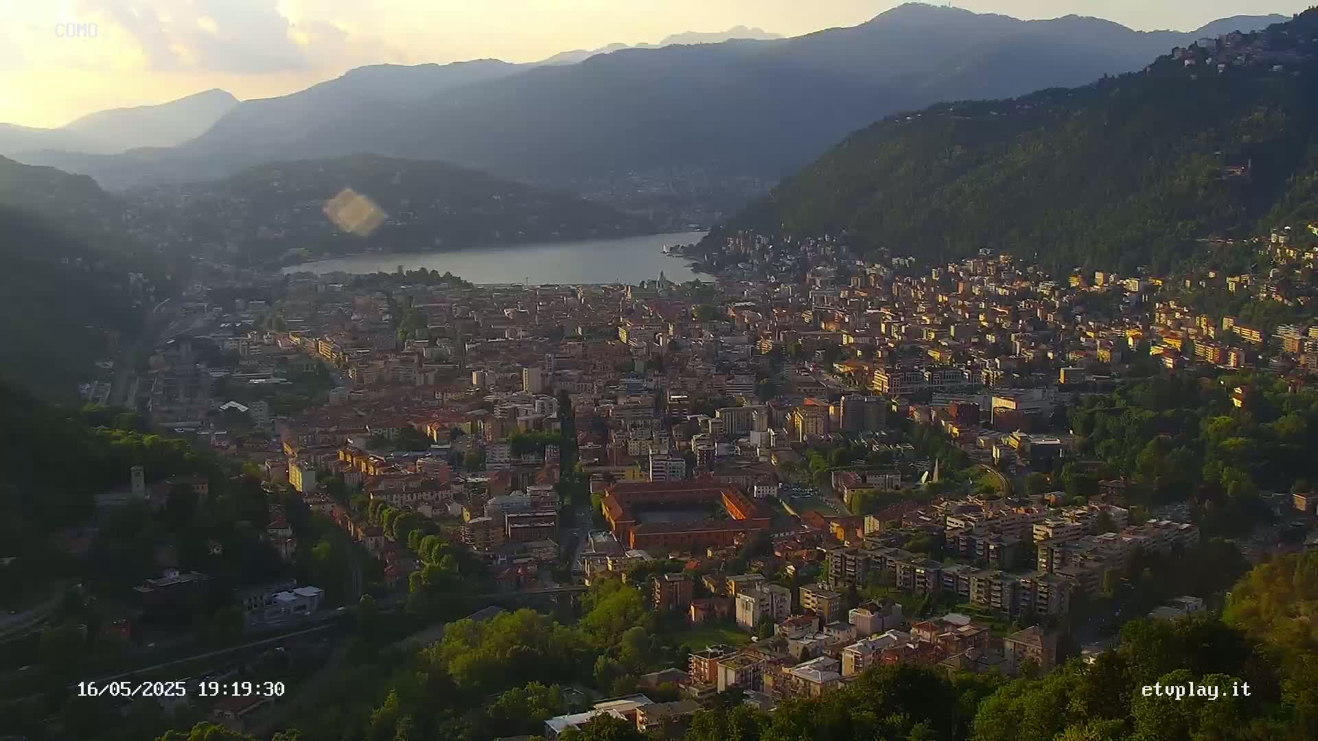 A sprawling city nestled between mountains and a lake, bathed in the soft light of dusk.