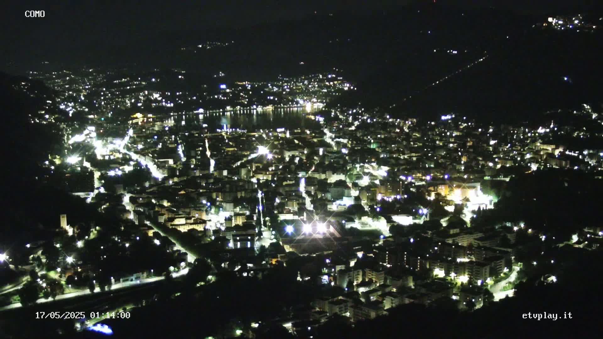 A nighttime, high-angle view of a city illuminated by lights, situated near a body of water.