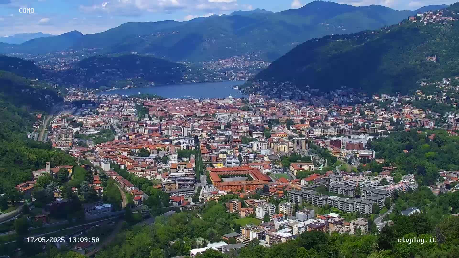 A sprawling city nestled in a valley between mountains, overlooking a lake under a partly cloudy sky.