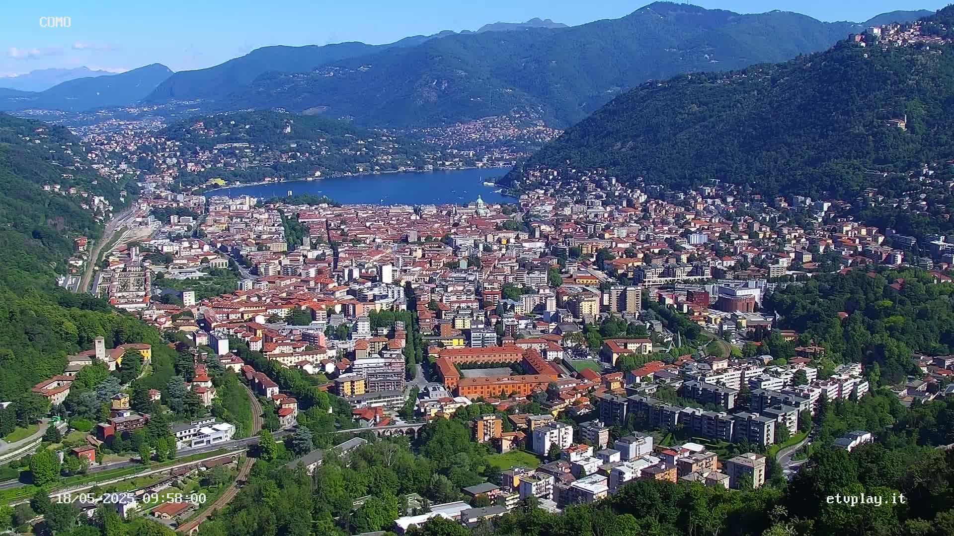 A sprawling city nestled in a valley between mountains, next to a lake, under a clear blue sky.