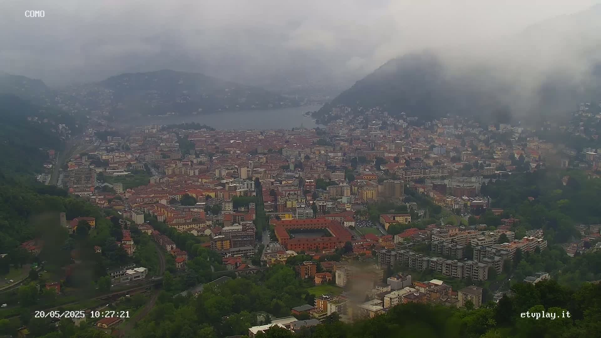 A sprawling city nestled between hills and a lake is shrouded in fog.